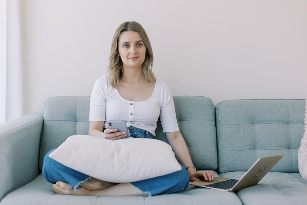 Women sitting on a blue sofa next to her laptop for a branding photoshoot.