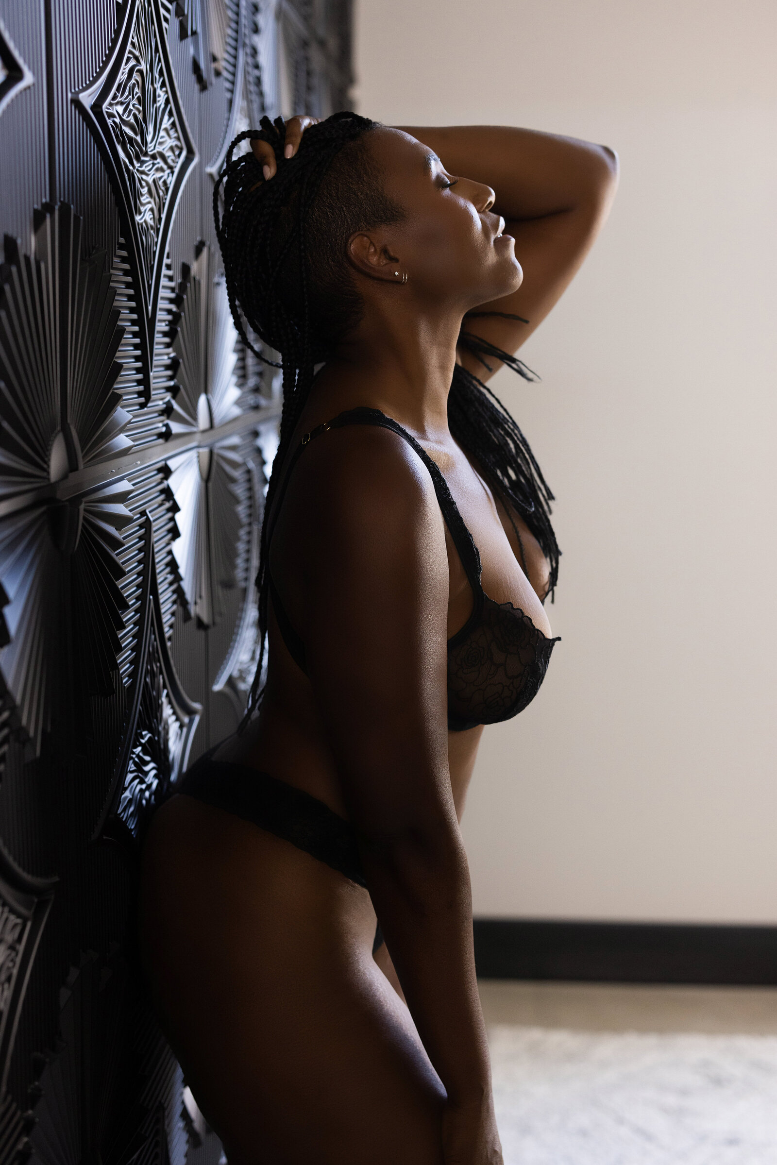 black woman leaning against a wall in a black bra lingerie set posing for a boudoir image