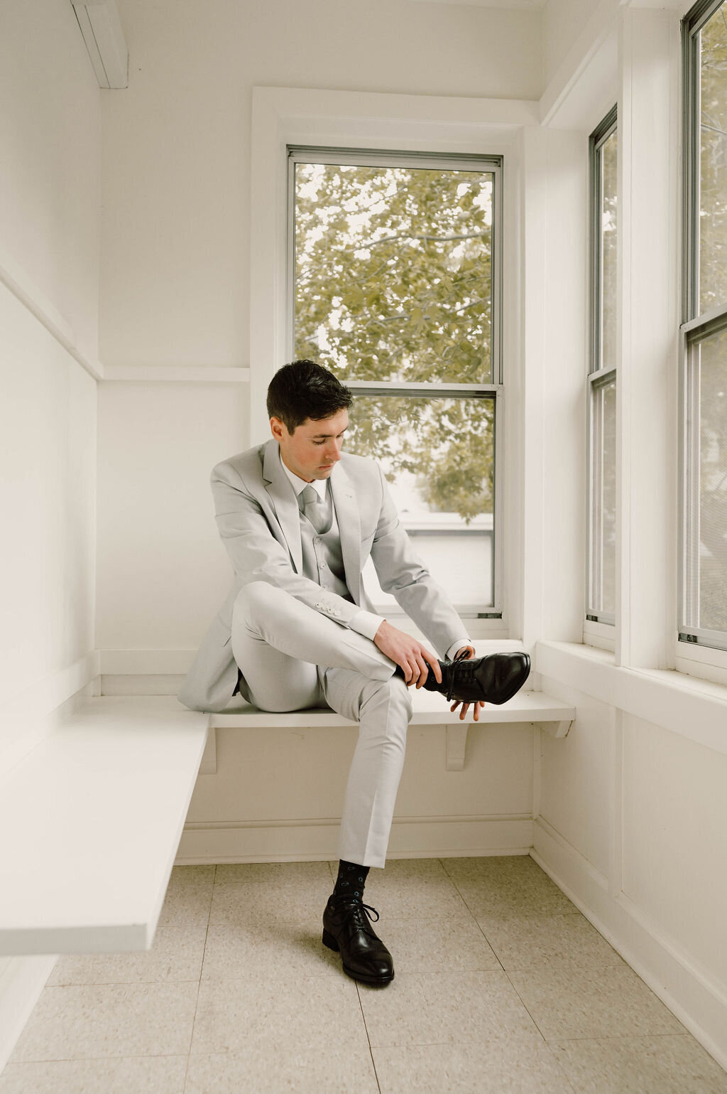 Groom wearing a gray suit putting black loafers on in getting ready photo
