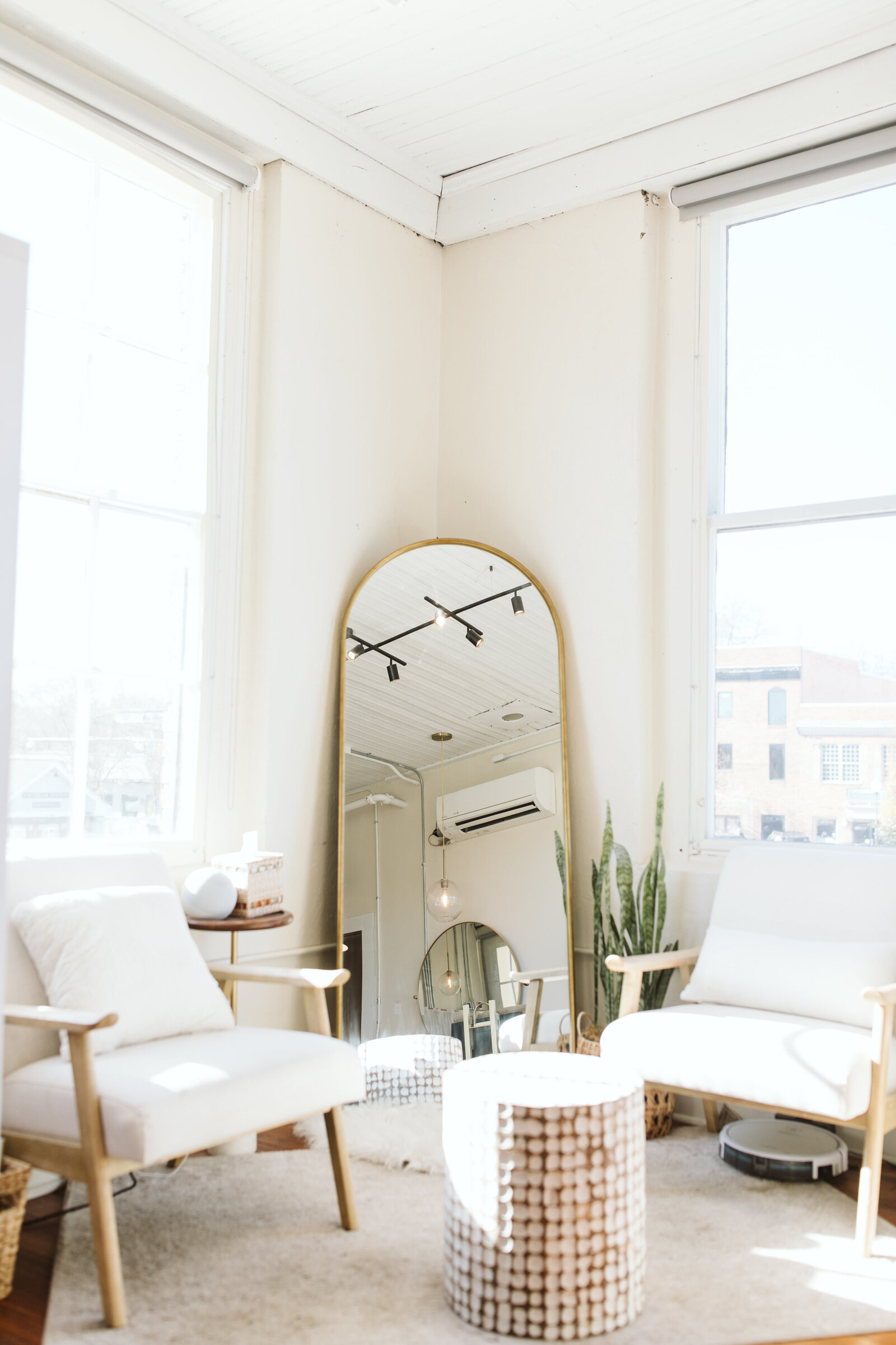 Bright hair salon interior with cozy armchairs, wooden floors, and a large arched mirror reflecting a serene atmosphere