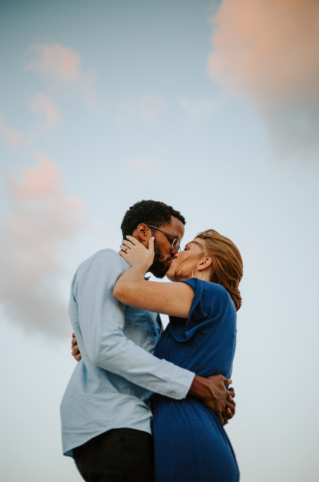 Couple holding in each other while kissing with the sky in the background during their Chicago engagement session