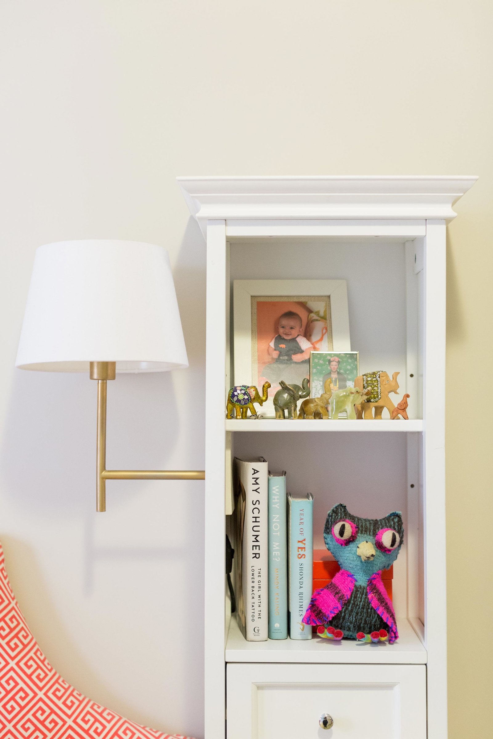 A bookcase with a gold sconce with white shade attached.
