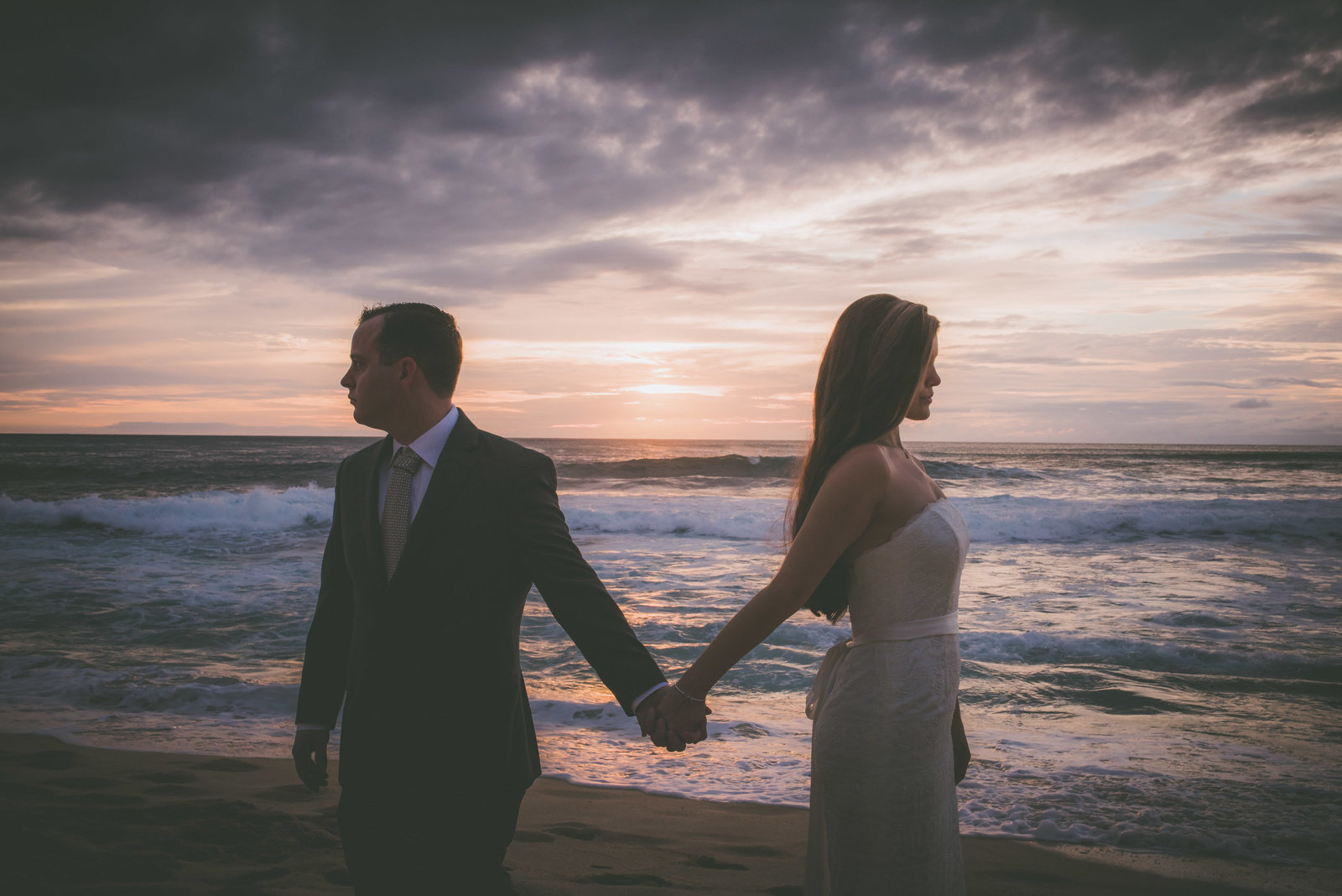 A couple hold hands during sunset on a Oahu beach.