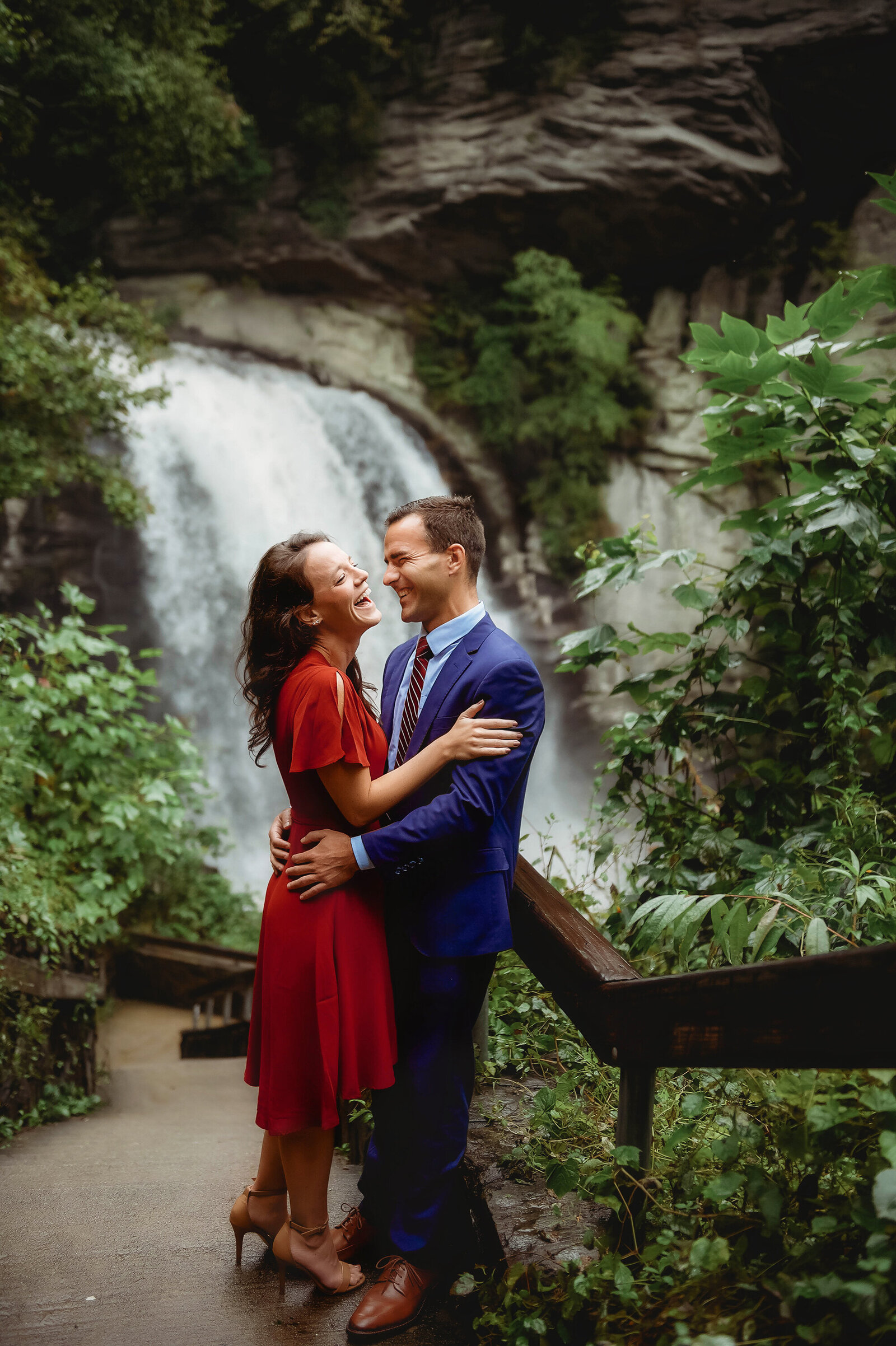 Couple laughs  in front of Looking Glass Falls while posing for Engagement Photos near Asheville, NC.