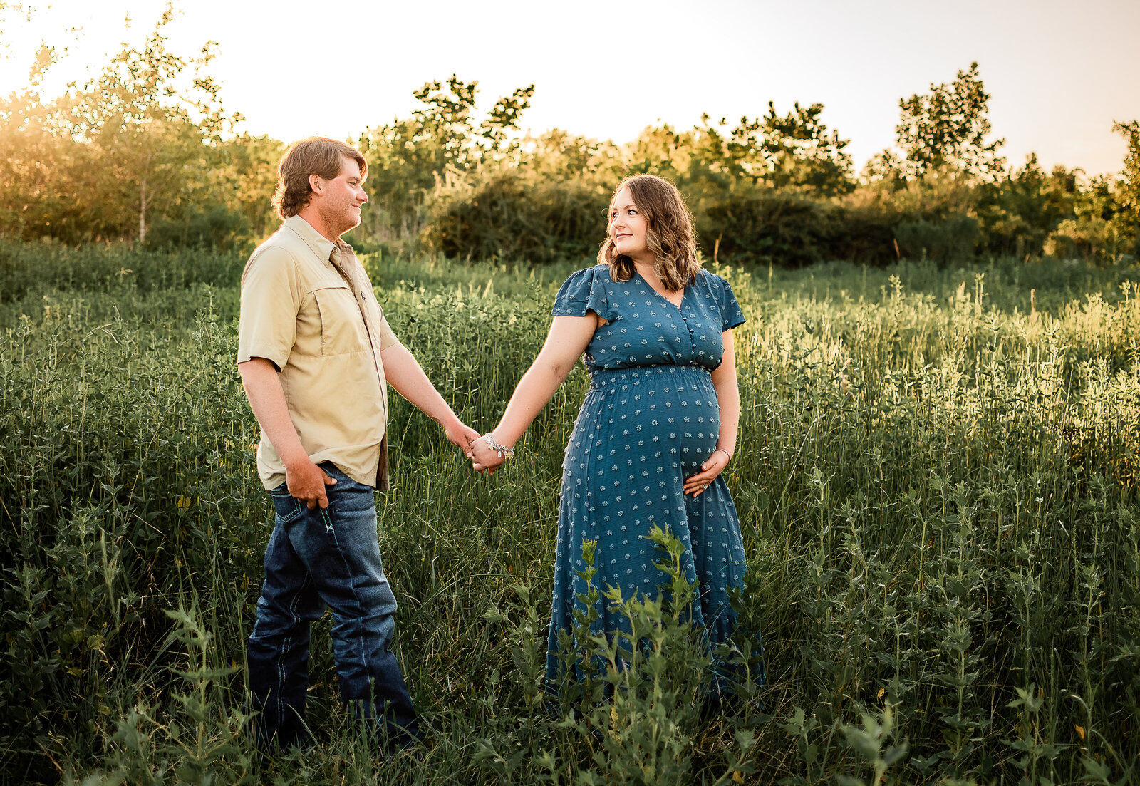 An expectant couple walks through a field of tall grass and flowers in Webster, Texas.