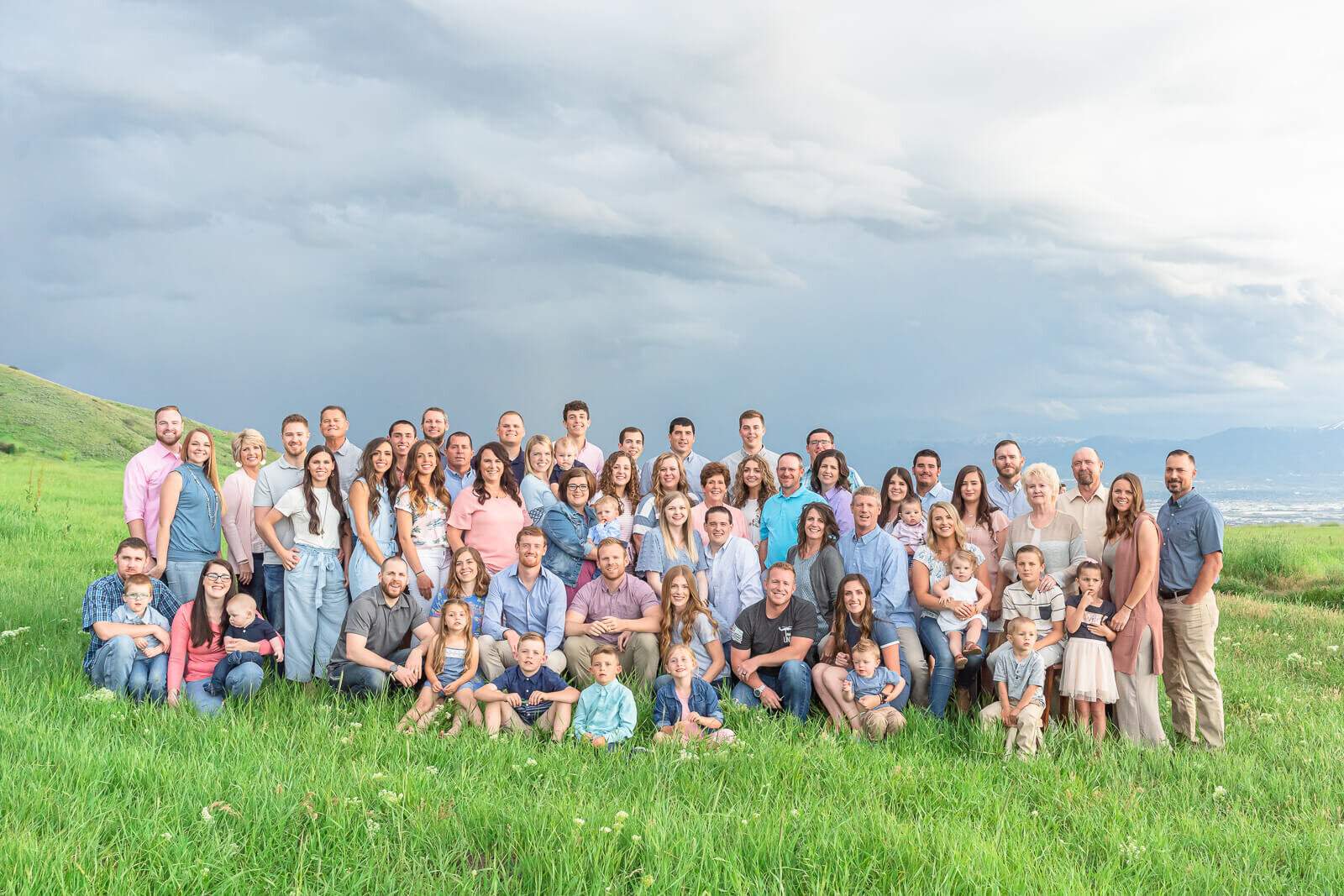 A large extended family gather together for portraits in a lush green field at Tunnel Springs in Salt Lake City