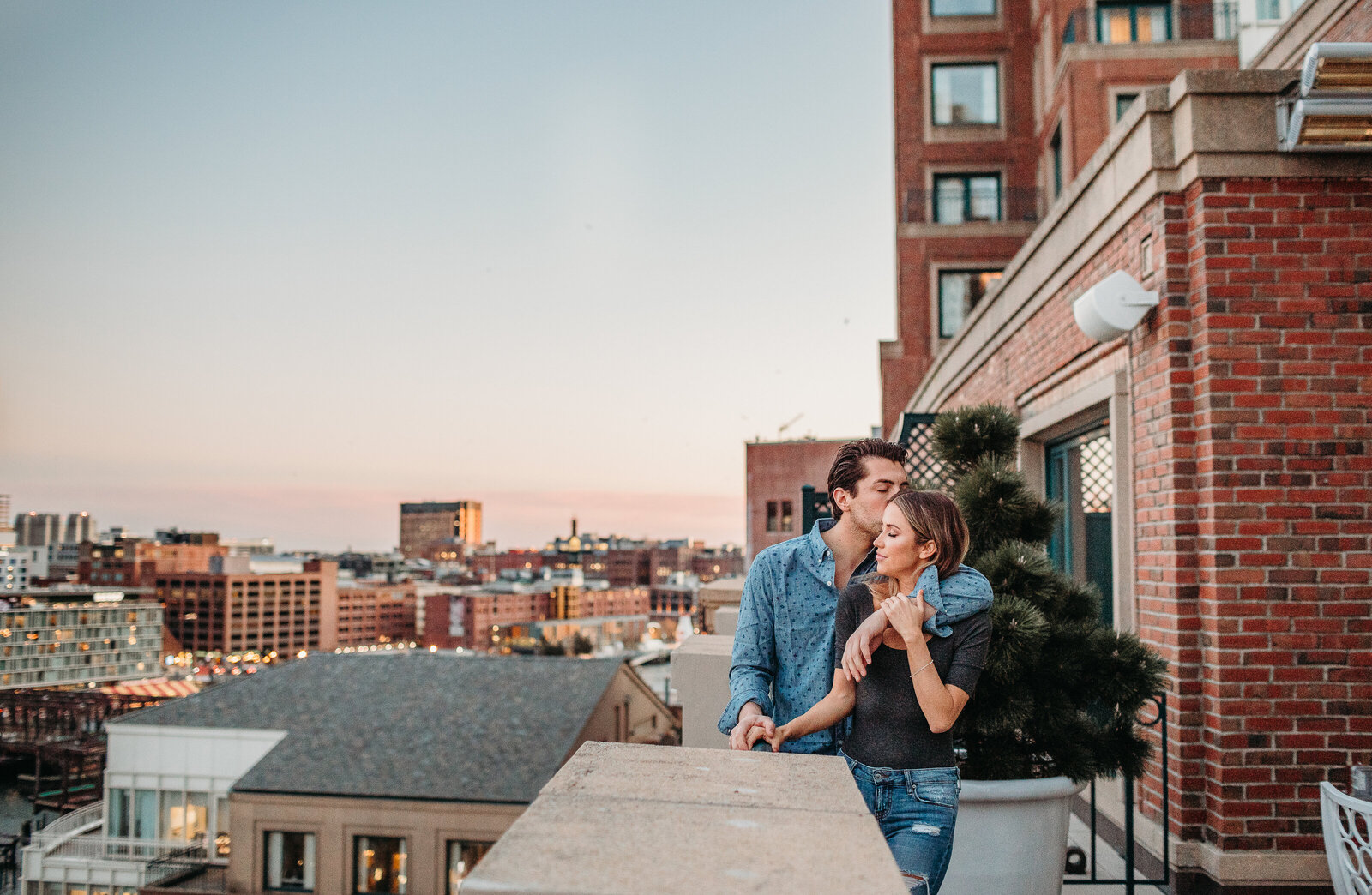 couple snuggles on rooftop desk in boston at sunset