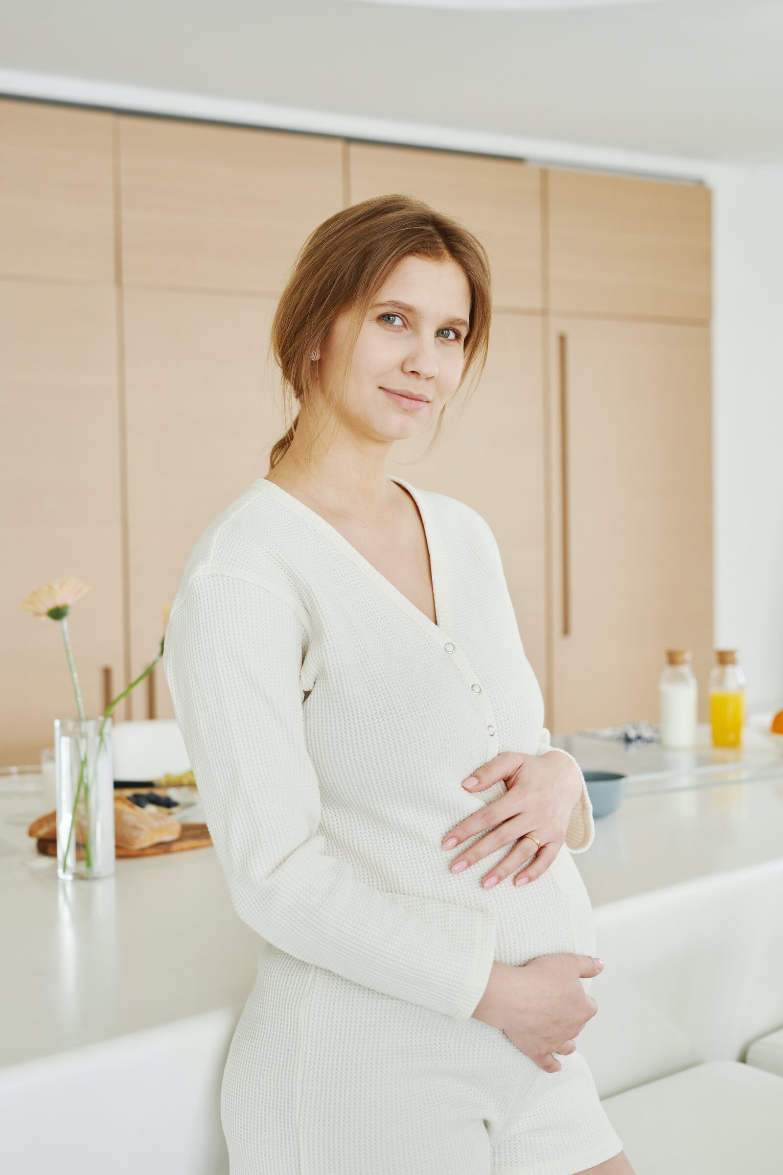 Prengnant woman standing  at kitchen counter holding her belly.
