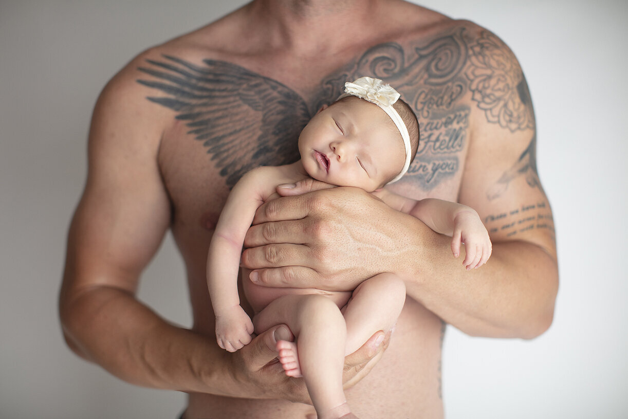 Newborn girl in her father’s hands showing tattoos.