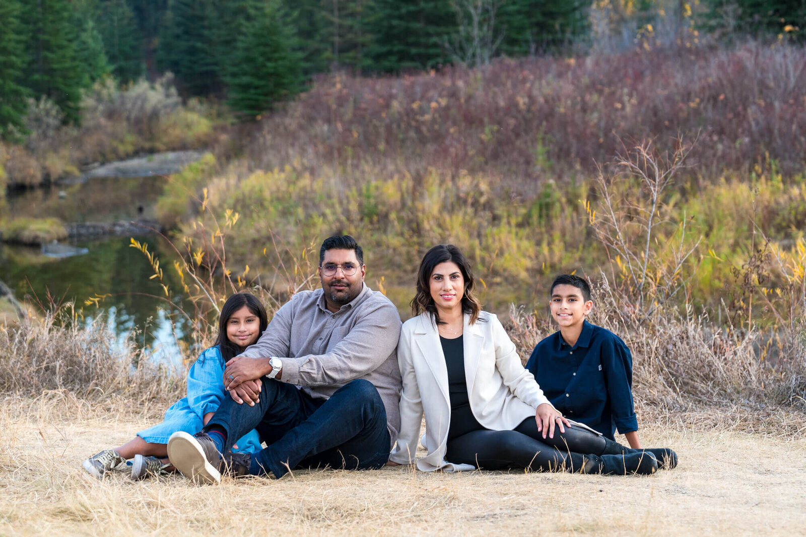 Family of 4 seated and posed infront of river