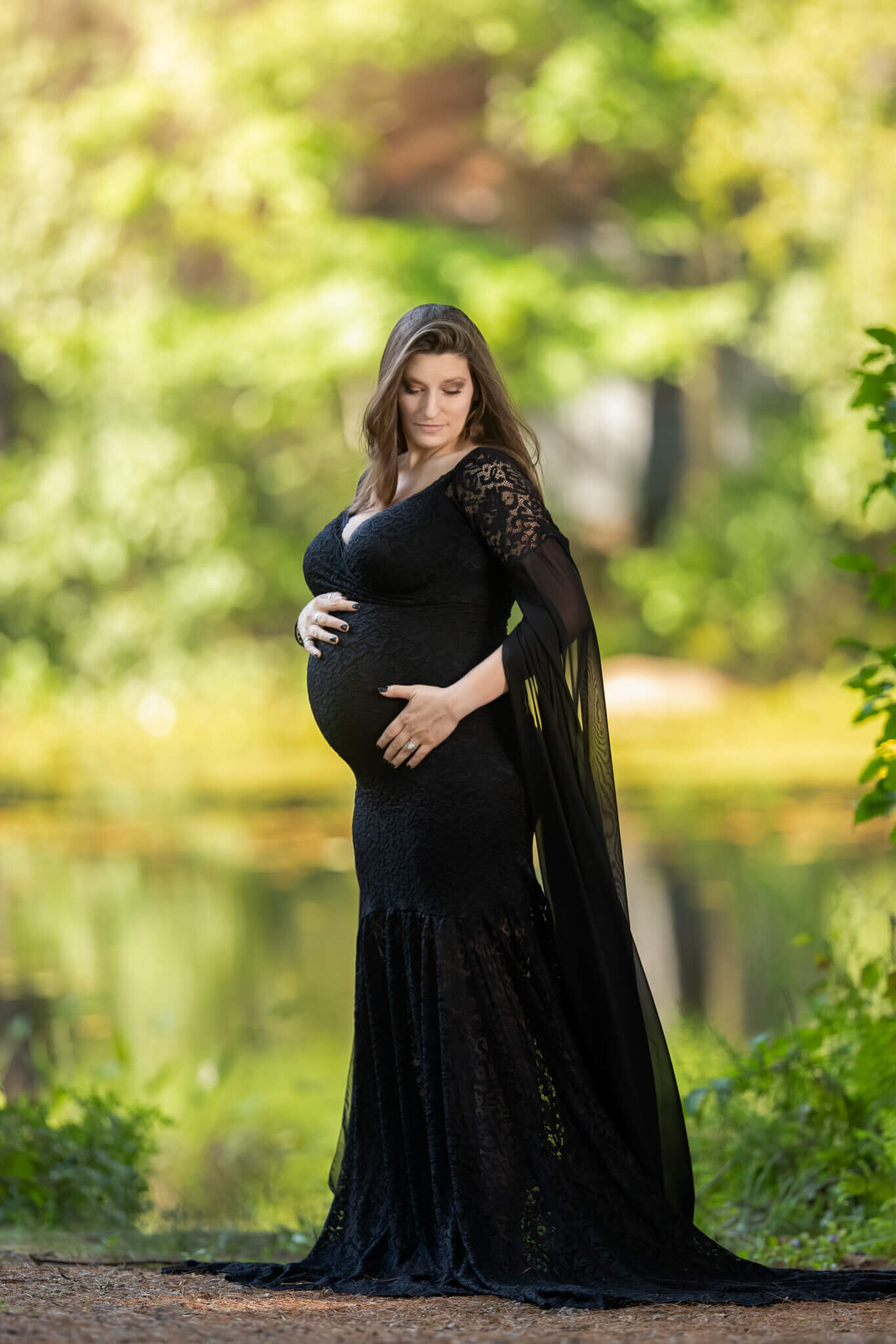 Pregnant mother in black gown with lace sleeves looking down at her baby bump