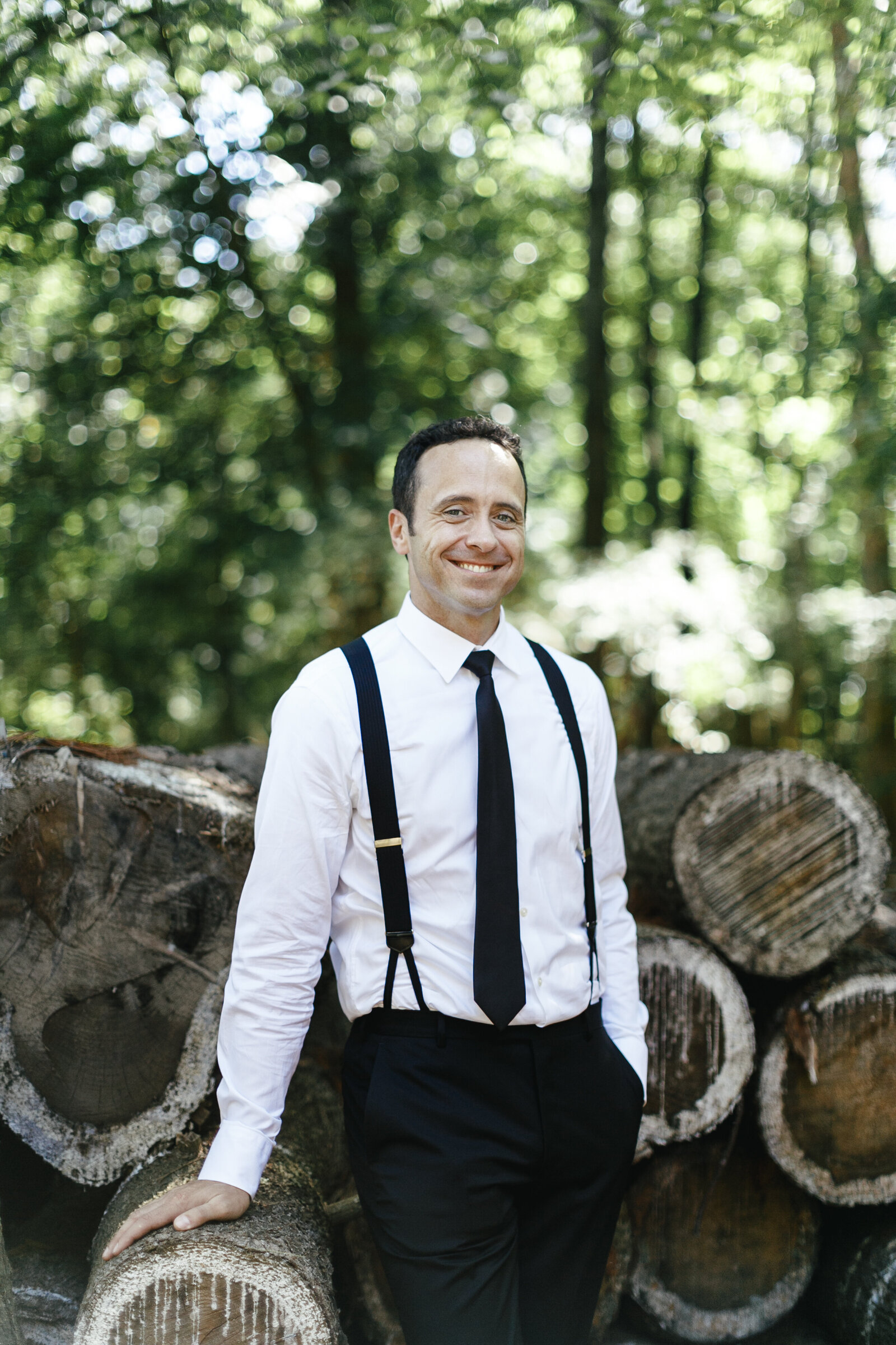 groom with suspenders at farm with wood pile