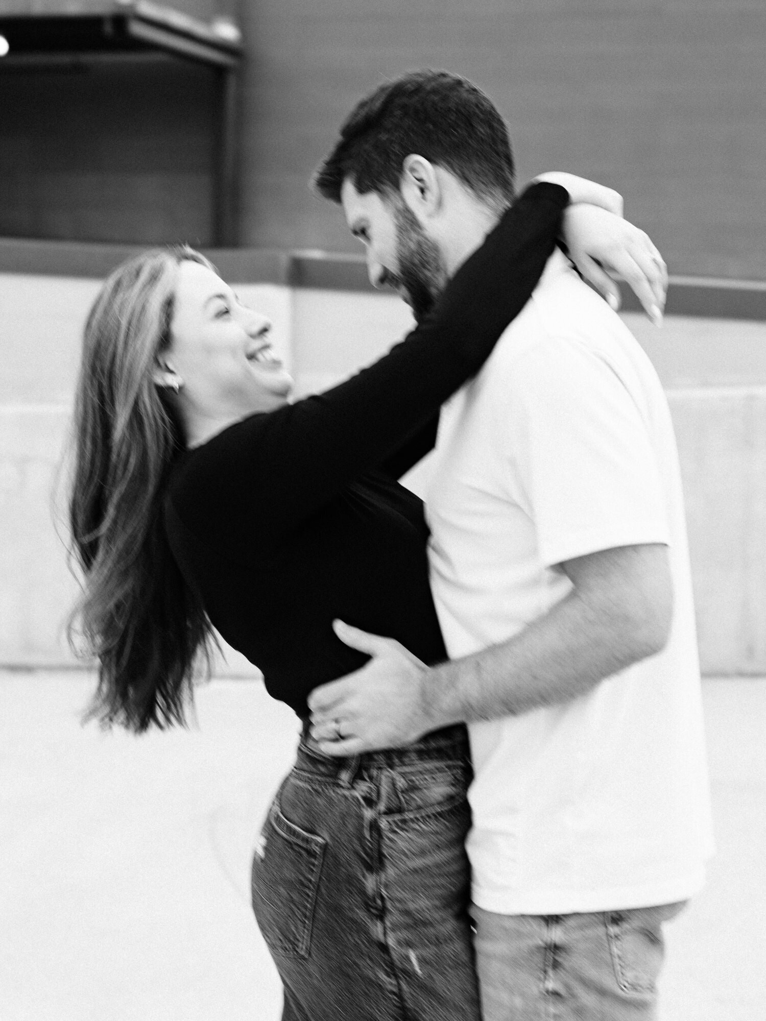 This image, taken by KD Captures, a wedding photographer in San Antonio, features a couple smiling at each other. The woman is wearing jeans and a black shirt and the man is wearing a white polo shirt and jeans. The photo is black and white, and has a motion blur effect.