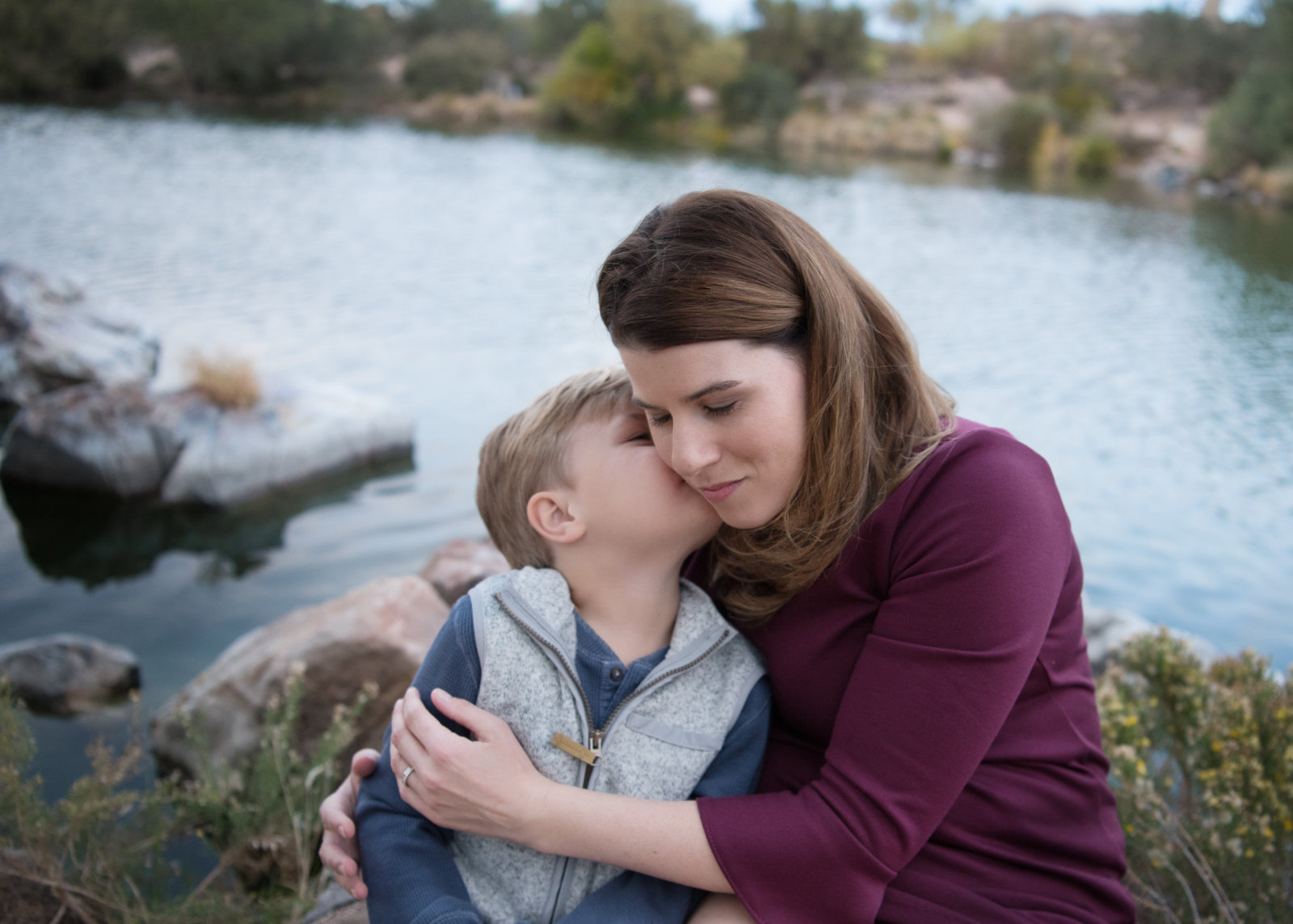 boy kissing his mom's cheek by a lake