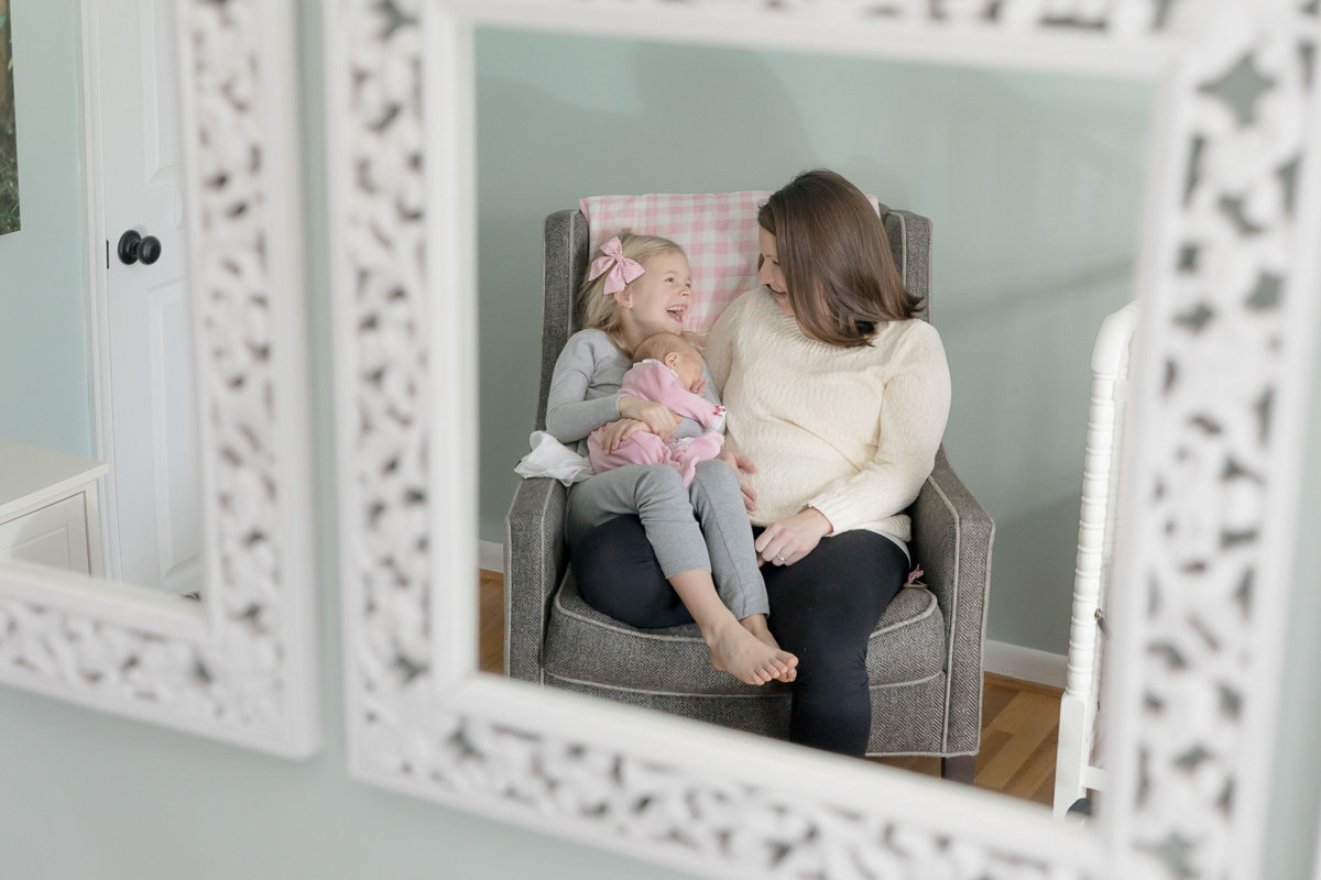 mom and daughter laugh together in mirror at lifestyle newborn photo session