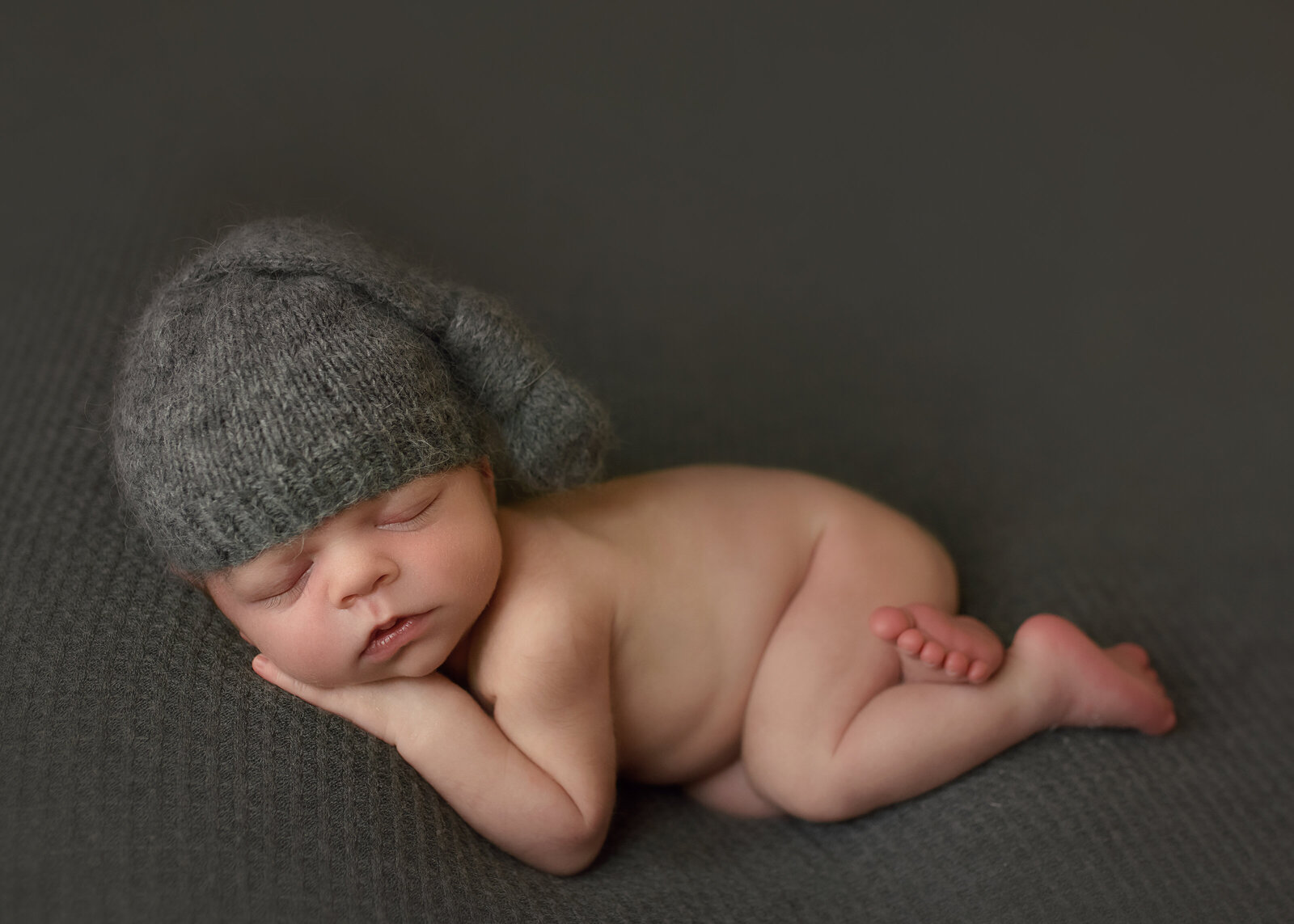 sleeping newborn baby boy laying on his stomach on a gray background with a gray sleeper cap on