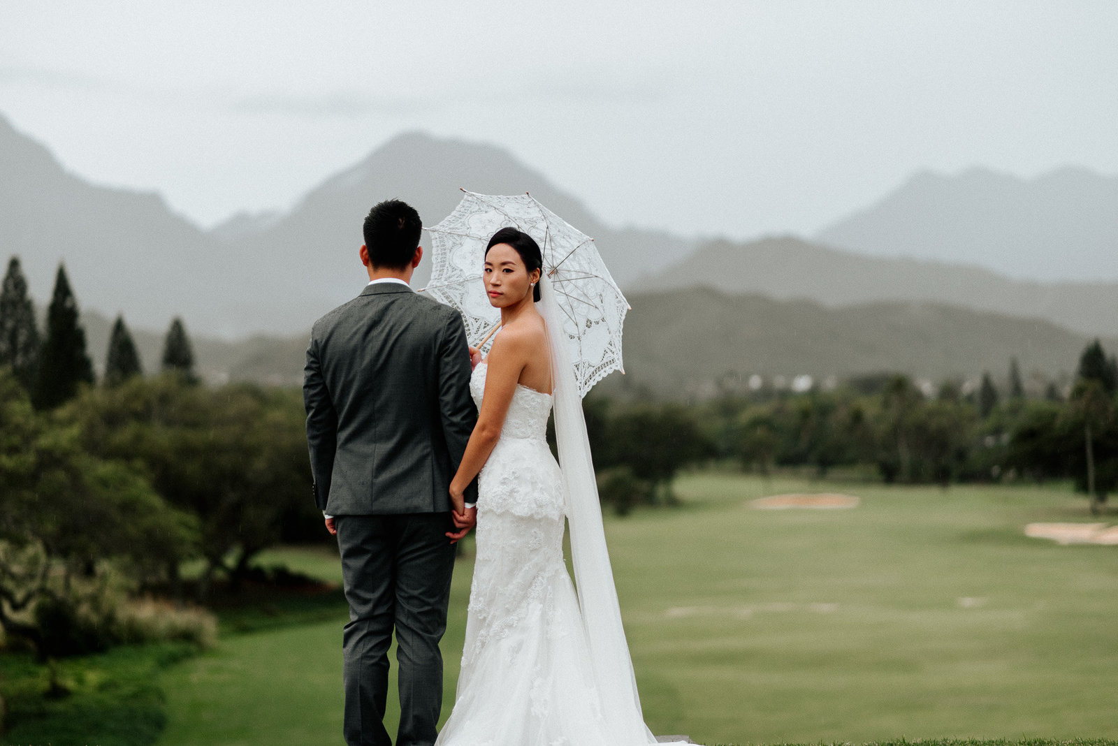 Destination wedding in Oahu Hawaii. Stunning asian bride looks back under lace umbrella.