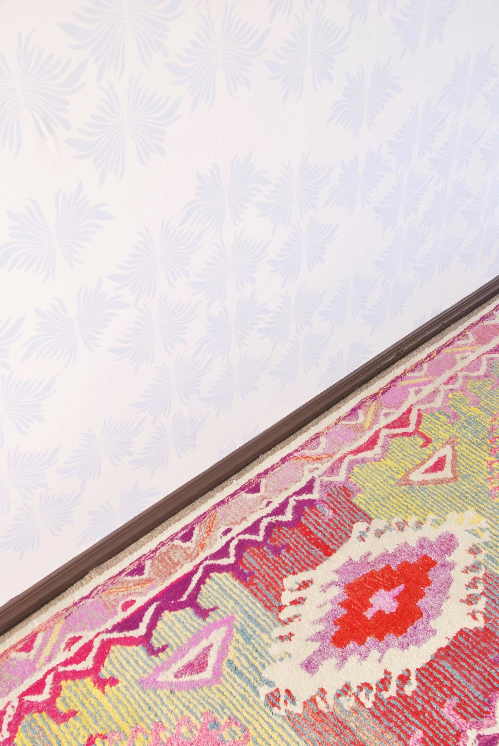 A colorful patterned rug next to an abstract wall papered wall.