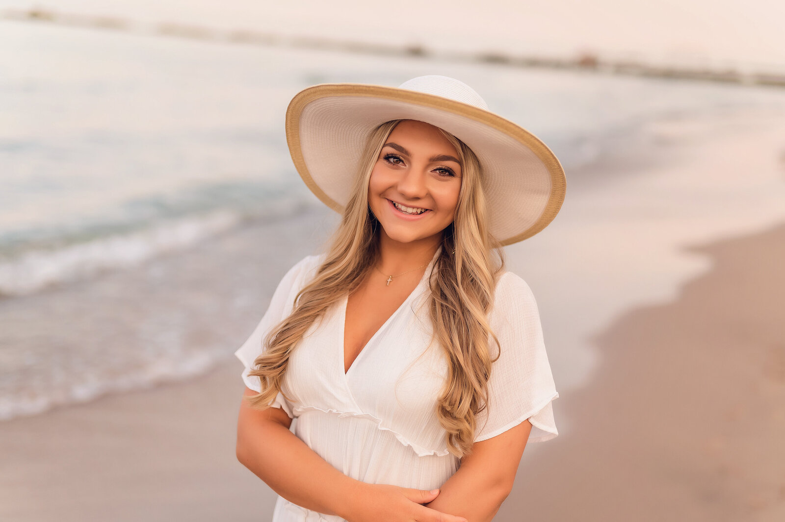 High school senior girl wearing a white dress and hat on the shores of Lake Michigan.