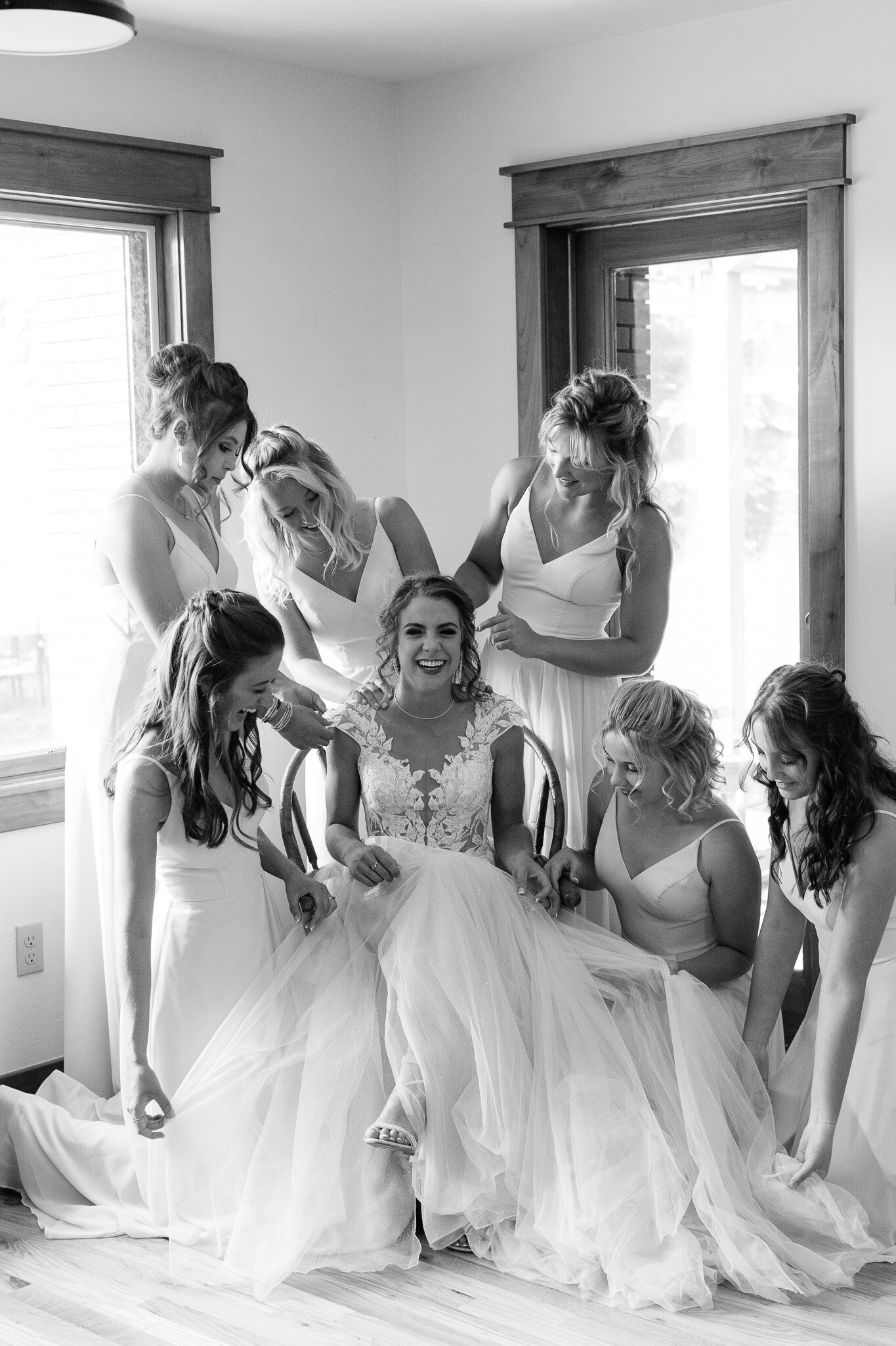 black and white image of laughing bride, bridesmaids hands on