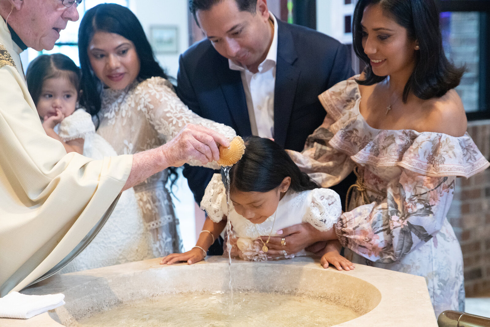 A young Latina girl bends over the font to get baptized Saint Augustine New City Rockland County baptism photographer Milestone Images