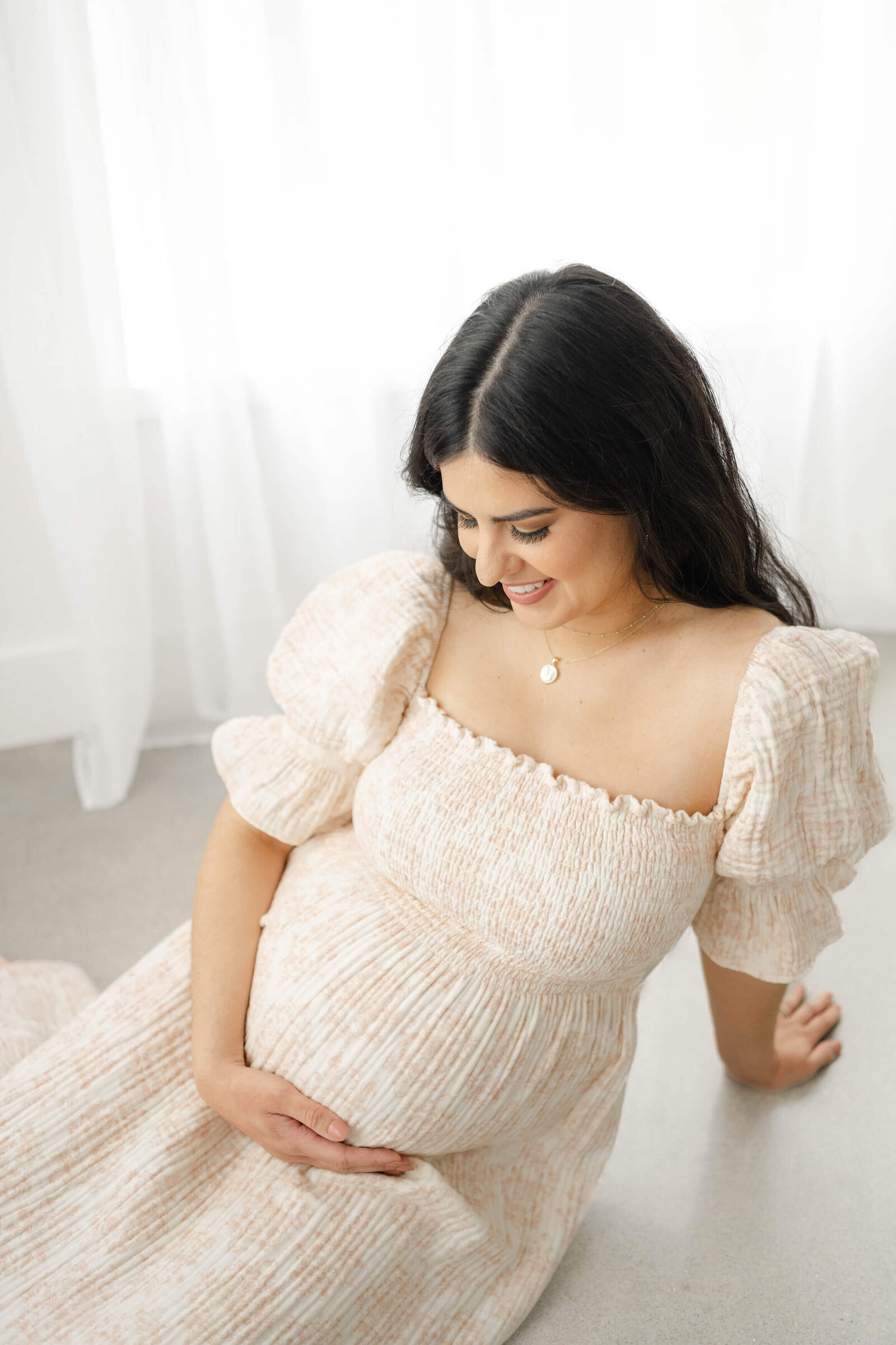 oklahoma mom to be wearing a pink dress as she sits on the floor looking down at her bump