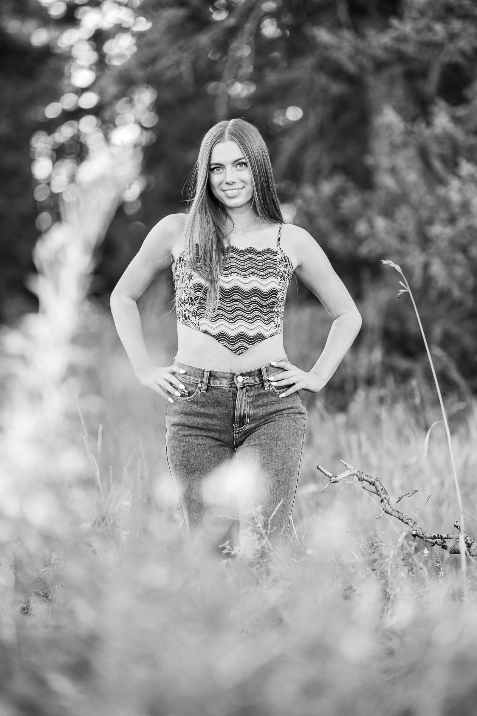 Senior stands with hands on her hips in tall grass for senior pictures