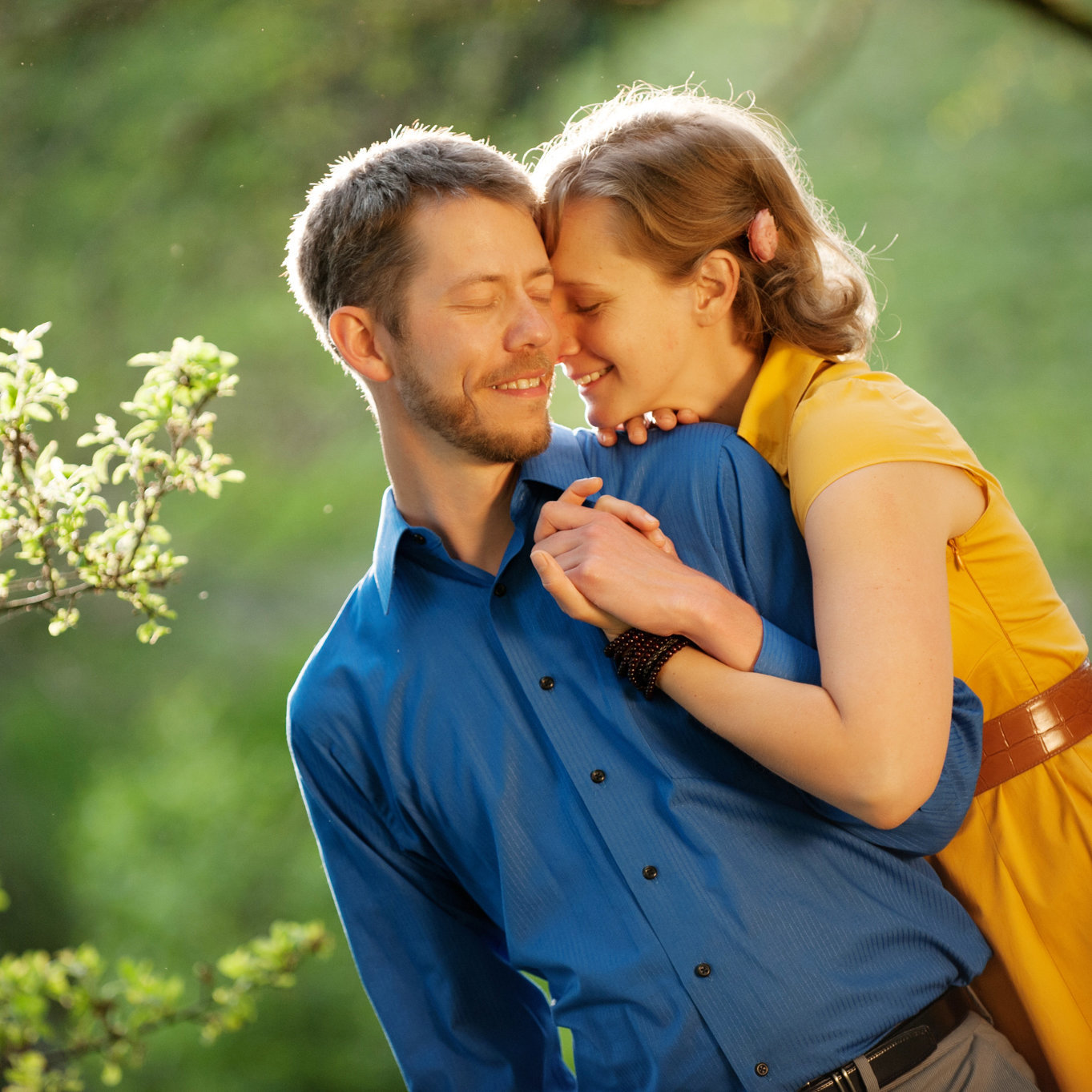 a woman in a yellow dress and a man in a bright blue shirt hug in the sunlight