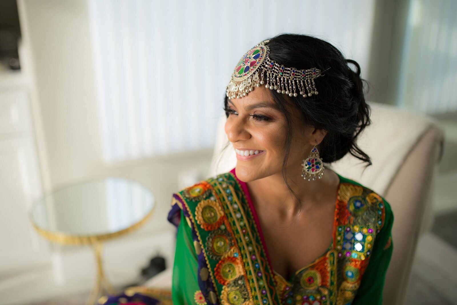 Bride dressed in traditional Afghan attire looks out the window smiling.  Photographed by wedding photographer in Sacramento, philippe studio pro.