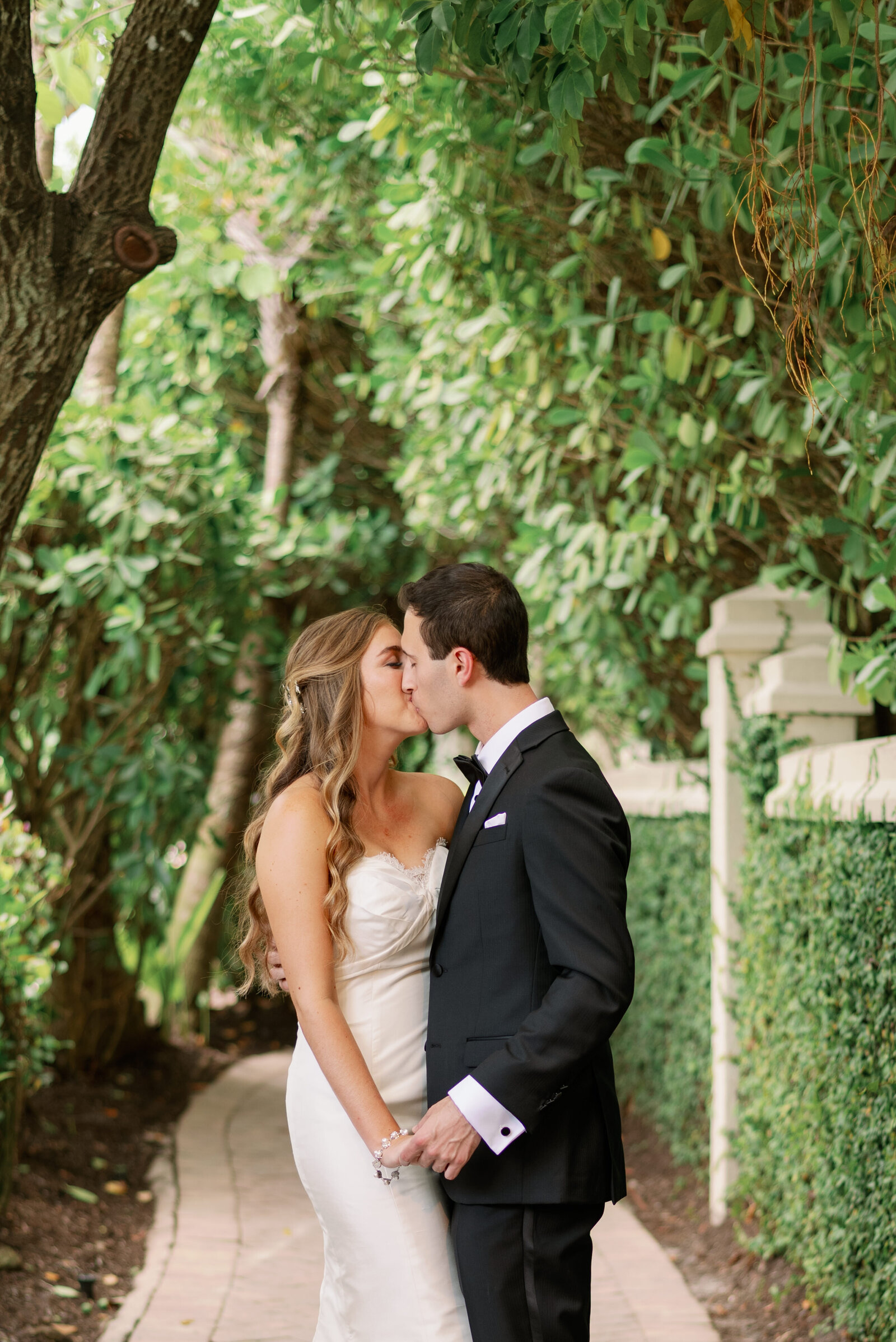 Bride and groom kissing and holding hands low on a secluded walkway