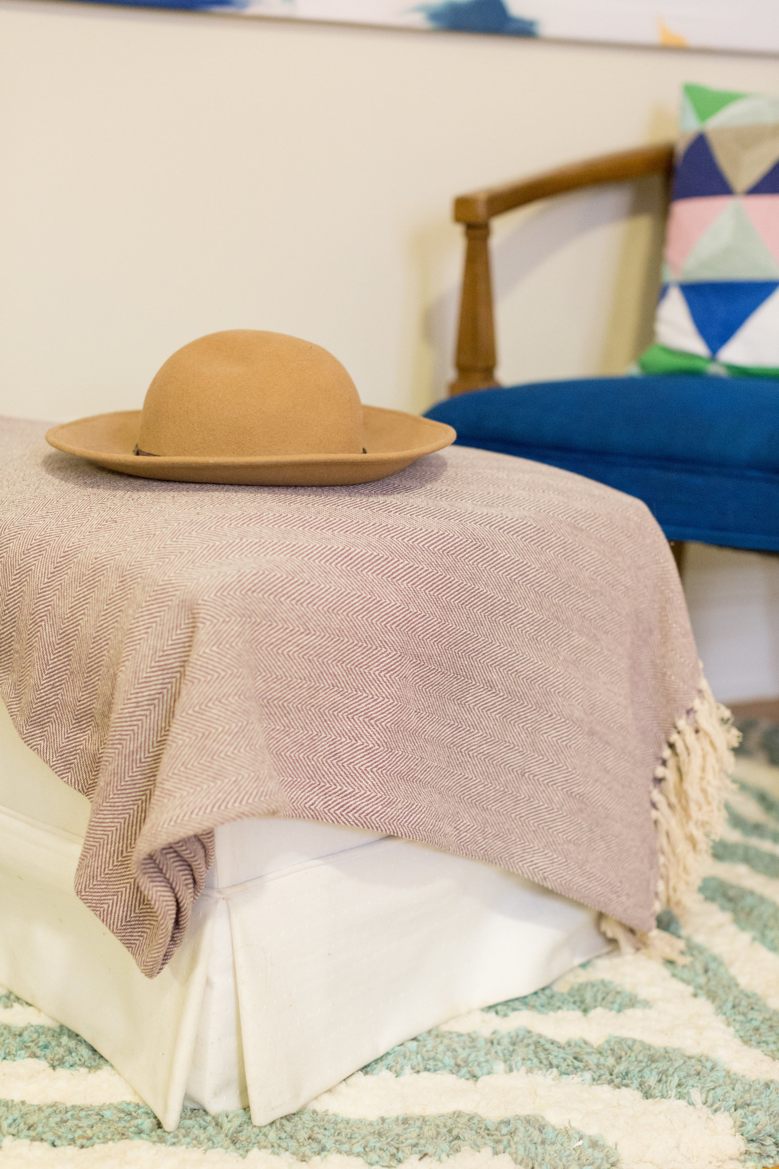 A tan sued hat on a blanket on an ottoman.