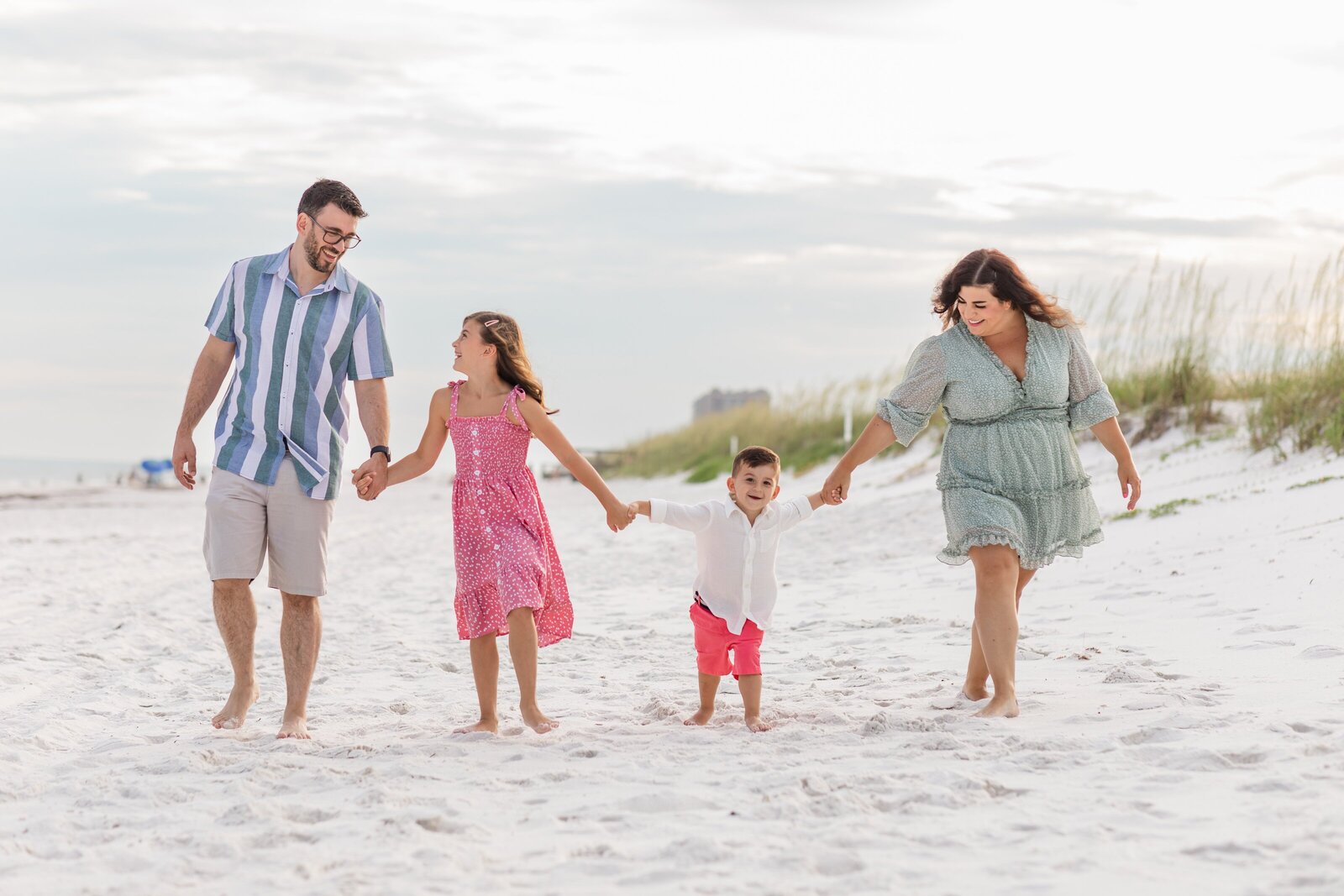 Pensacola Beach vacation family photo session .  Family holding hands walking down beach.