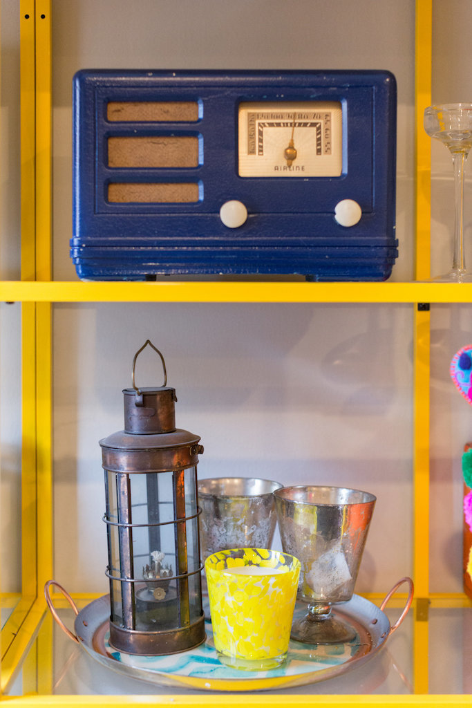 Yellow and glass shelves with a blue vintage radio, lantern, and dishes.