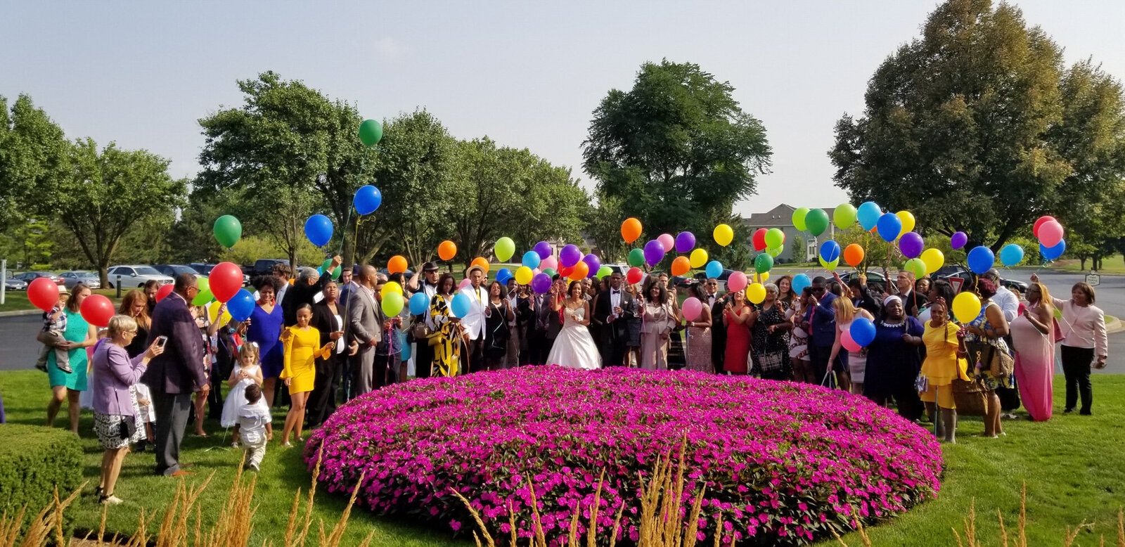 Wedding couple and guest holding colorful balloons with pink flowers in front
