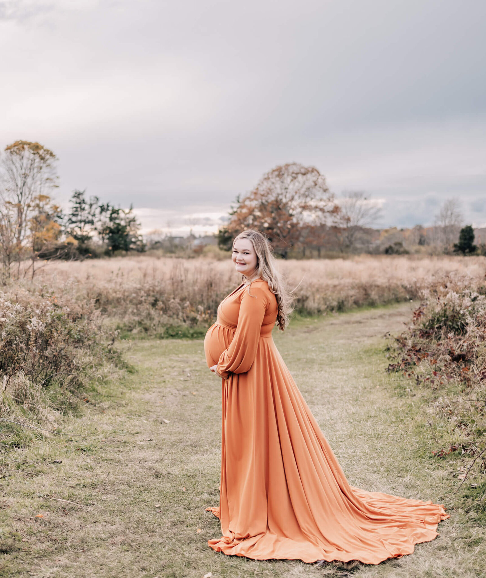 Pregnant woman in orange dress  in field at Harkness memorial state park