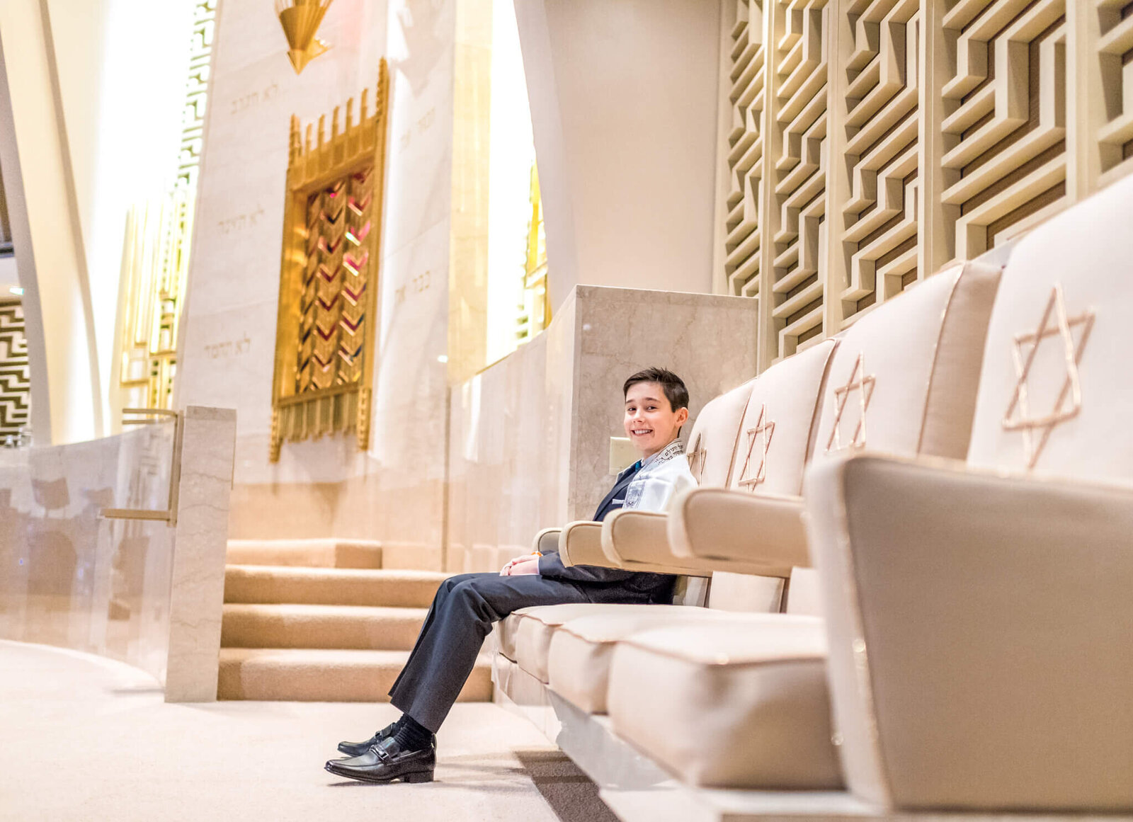 A teen boy sits in a chair on the bimah waiting for his readings