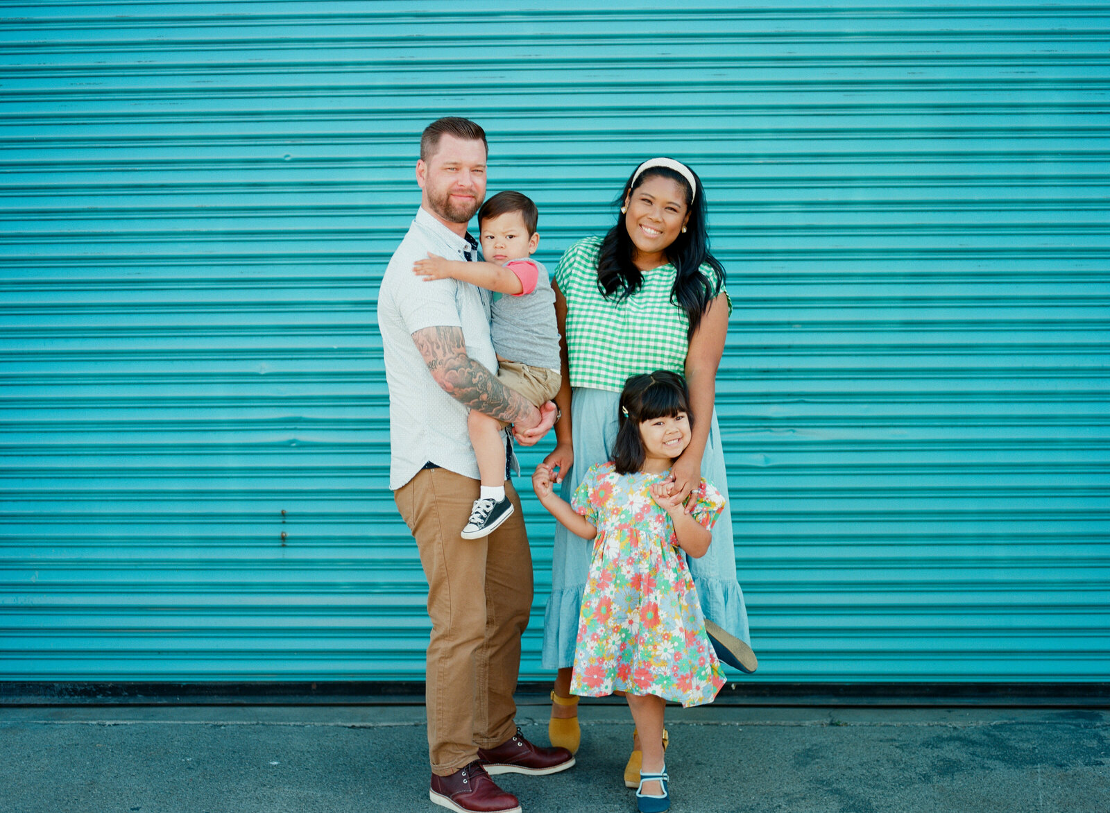 family of four standing together in front of an aqua blue metal wall