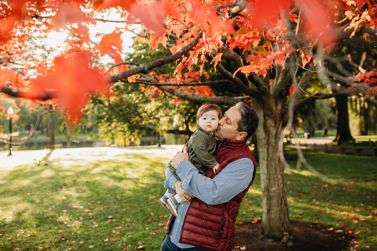 father holds baby girl under red autumn leaves during family photo session in boston