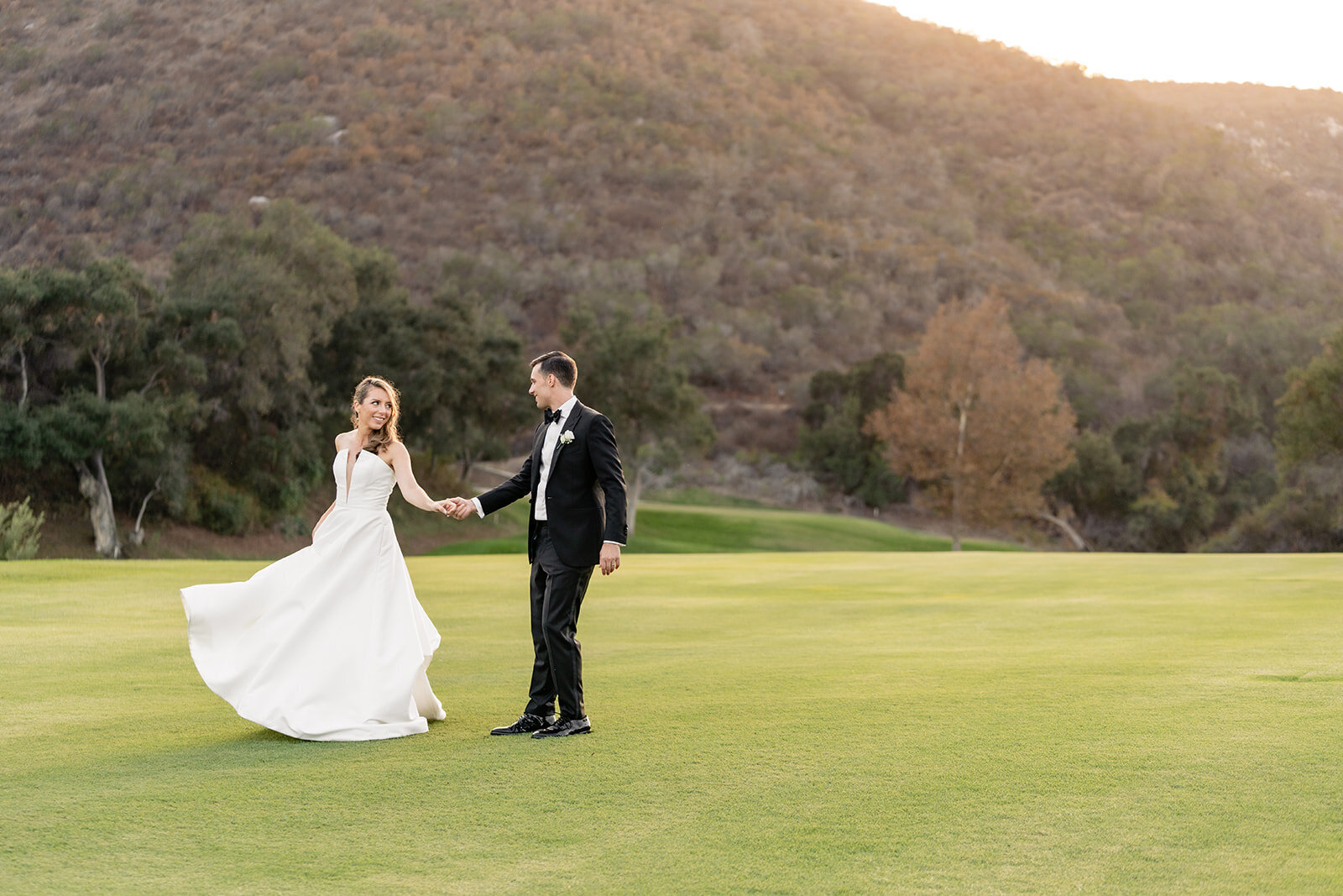 A bride and groom hand in hand on a golf course at Vista Valley Country Club.