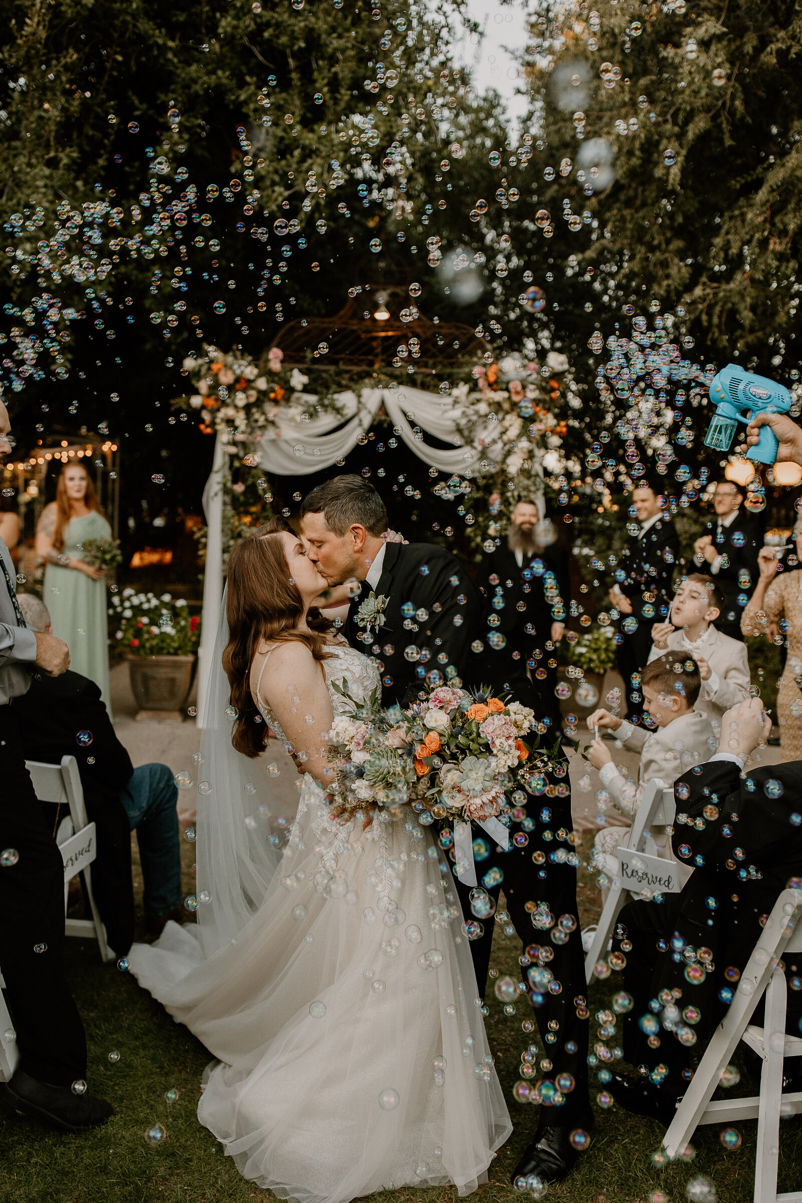 A wedding couple kissing while bubbles float all around them.