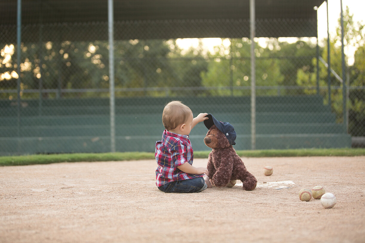 Baby boy with teddy bears on Austin baseball field.