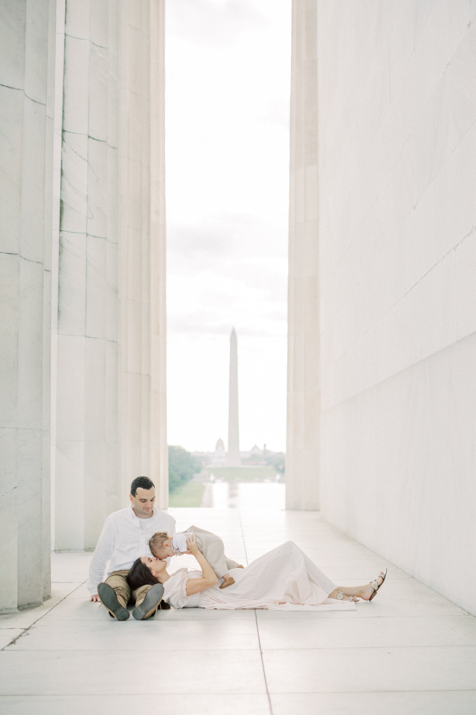 Mother lays in husband's lap and holds up infant son at Lincoln Memorial