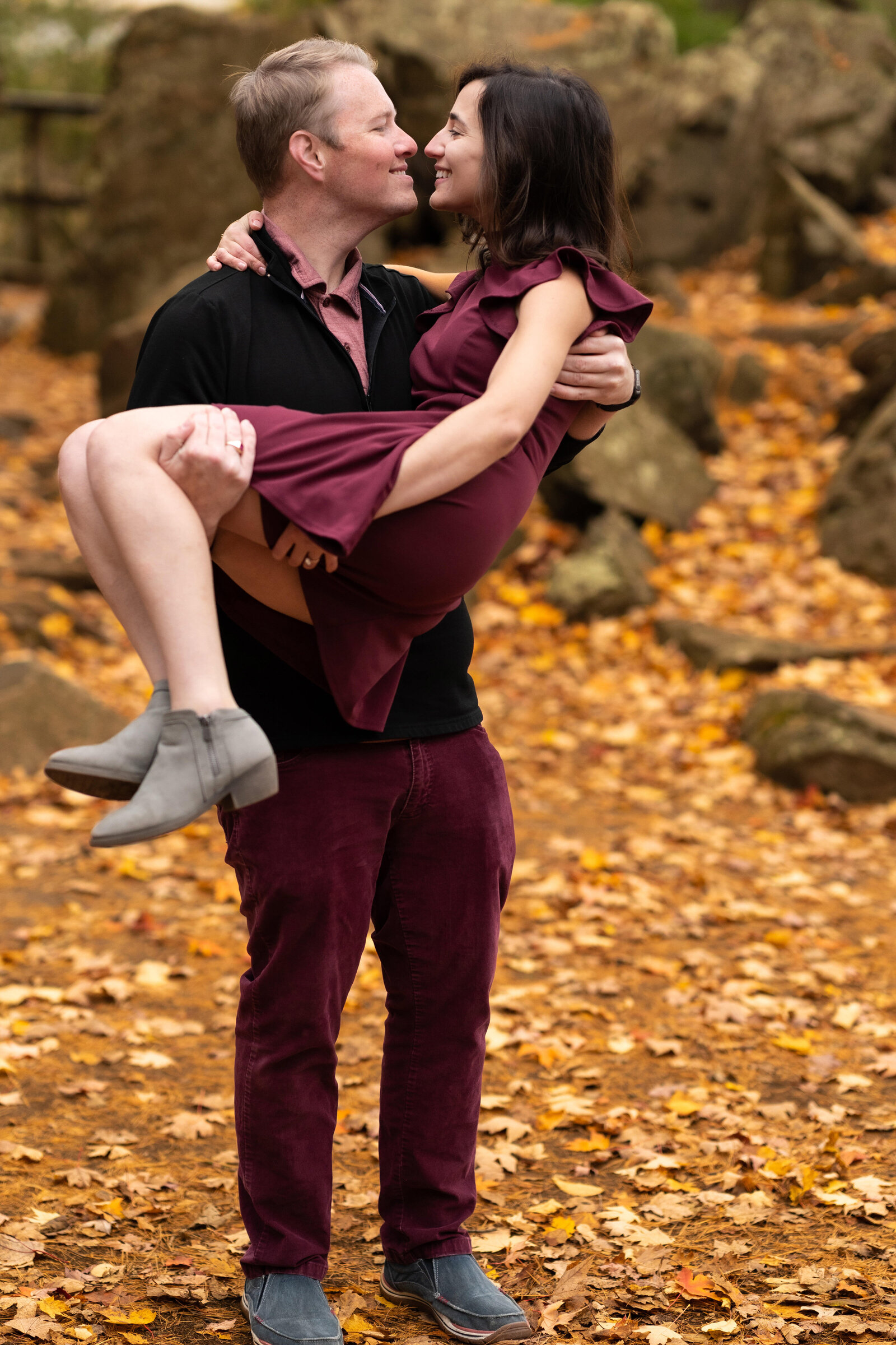 Man lifts and kisses woman in purple dress surrounded by leaves.