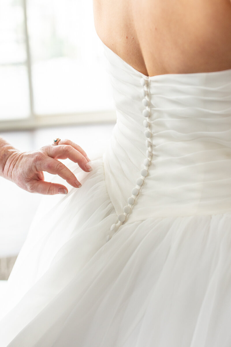 close up photo of mom of bride buttoning up bridal gown