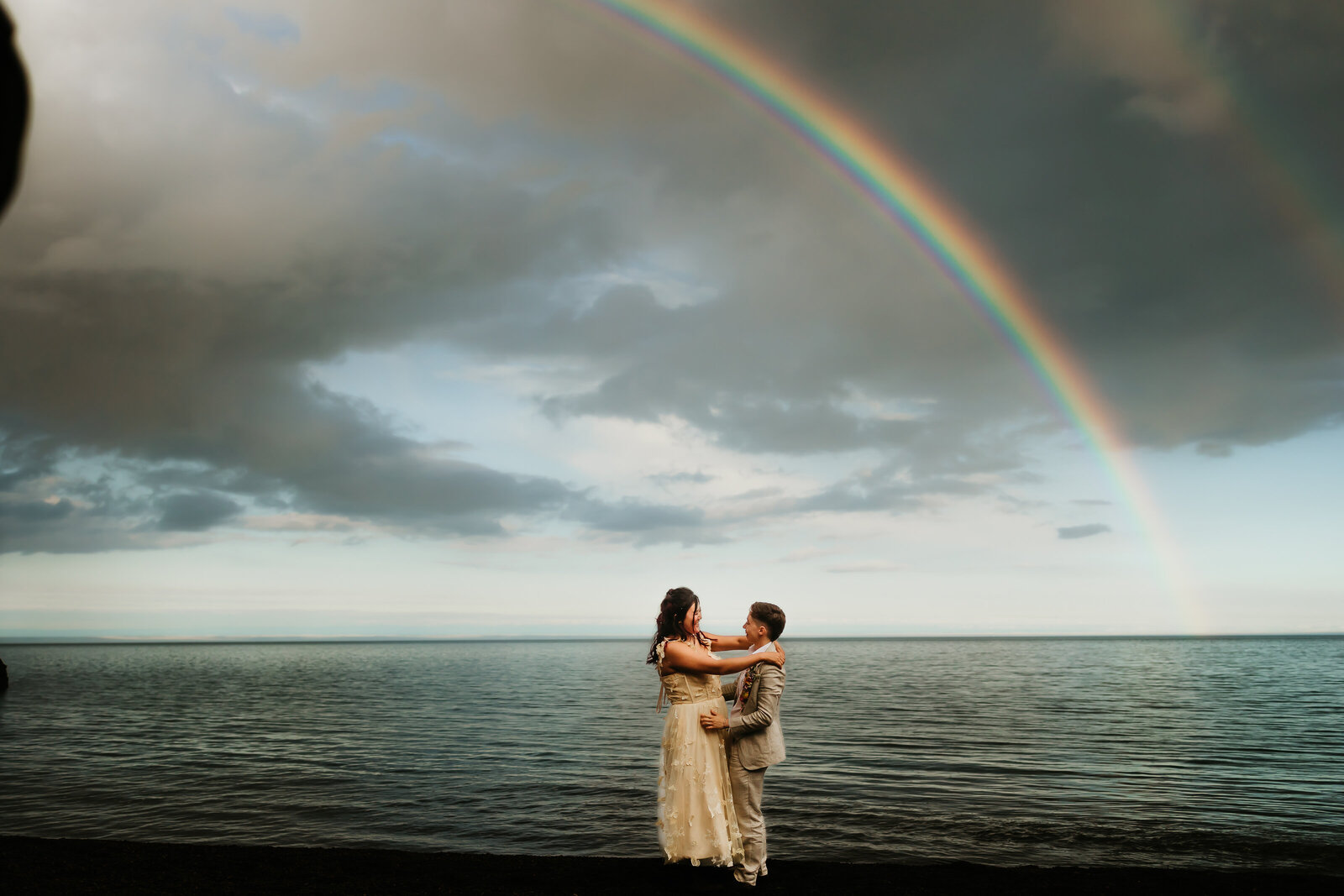 A couple kissing in a field with a rainbow in the background