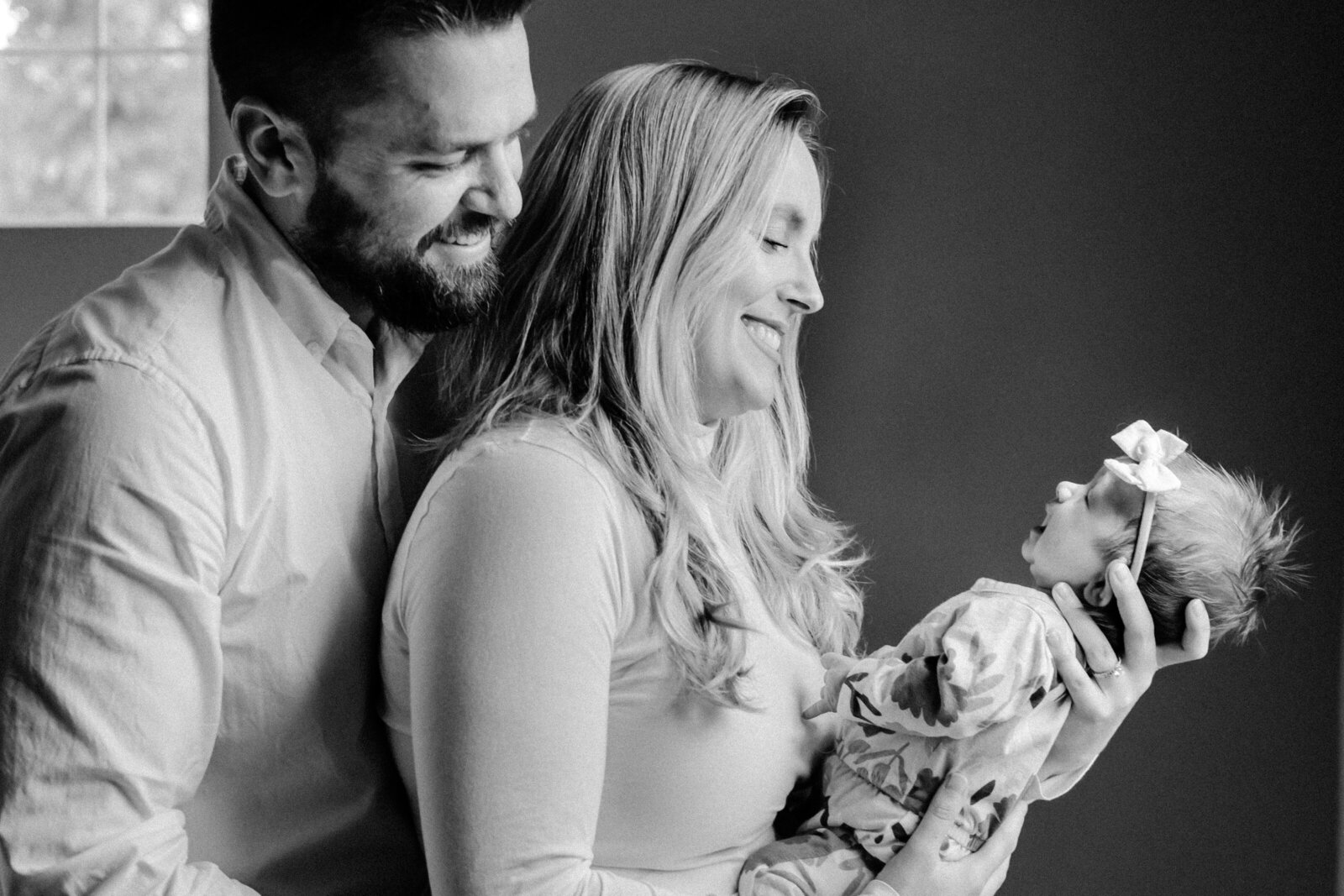 Mom and dad smile down at newborn daughter wearing big bow during newborn session in Tampa