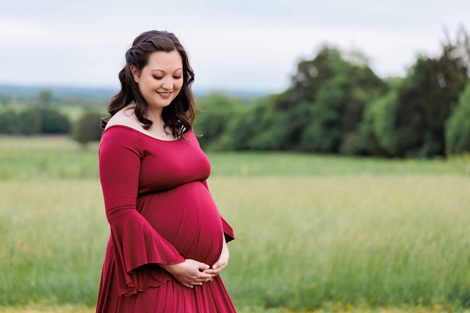 A beautiful pregnant woman in a red dress posing in a field in Manassas.