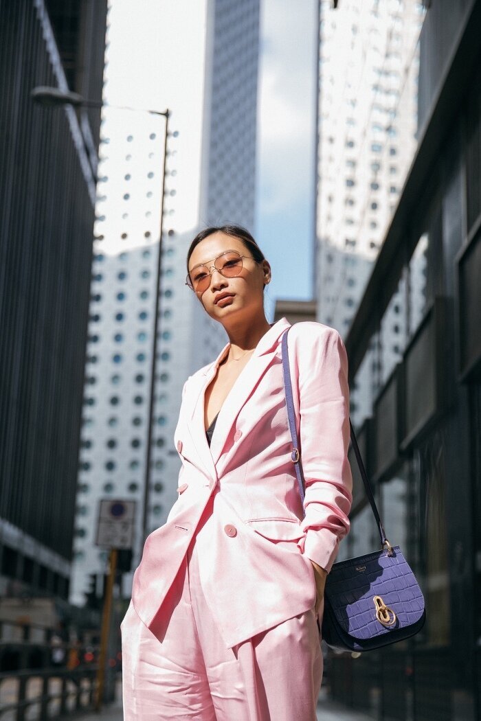 Woman wearing pink suit and purple bag with city in the background