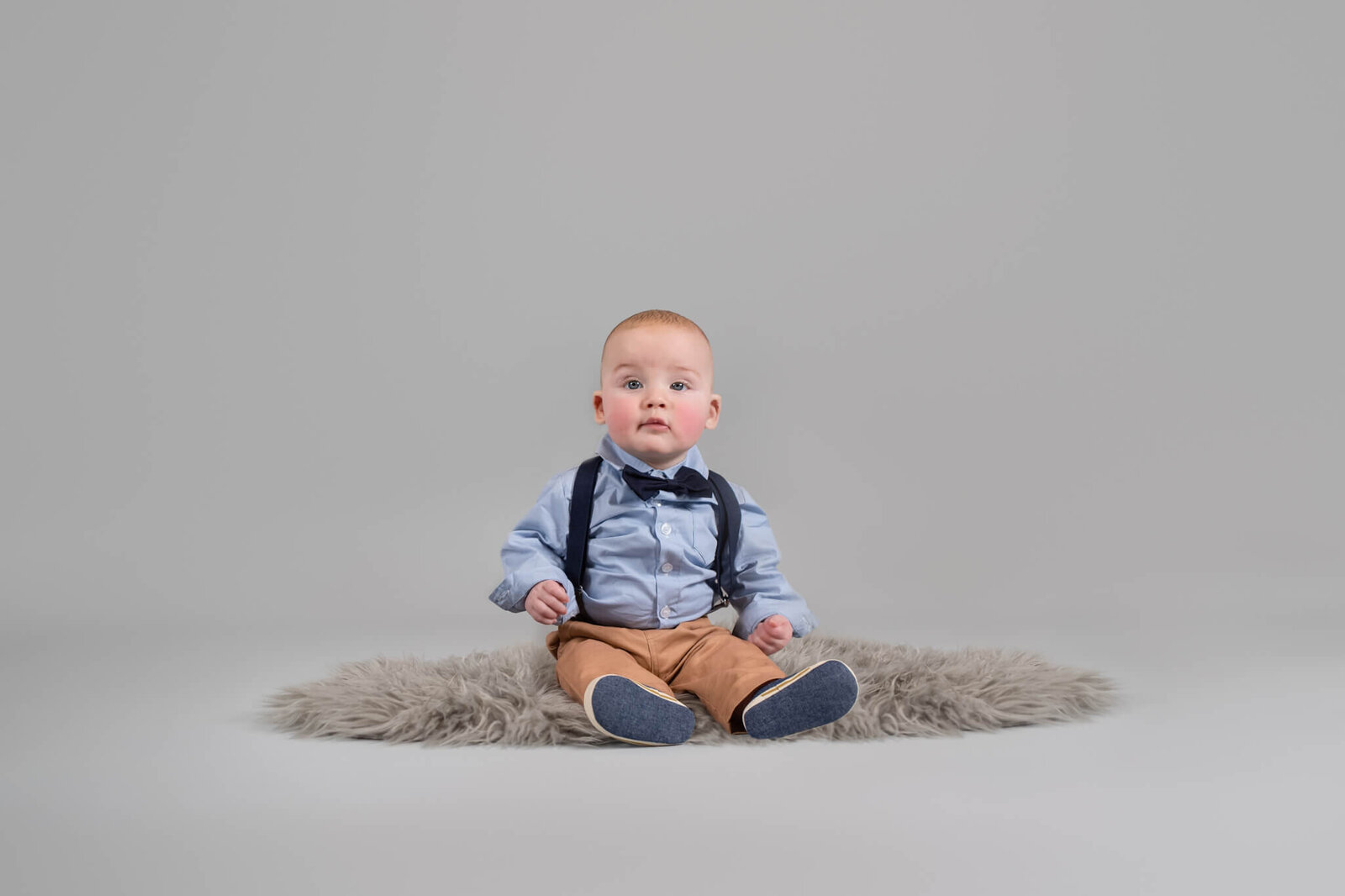 Six month sitter session of little boy on gray background wearing a suit and navy overalls