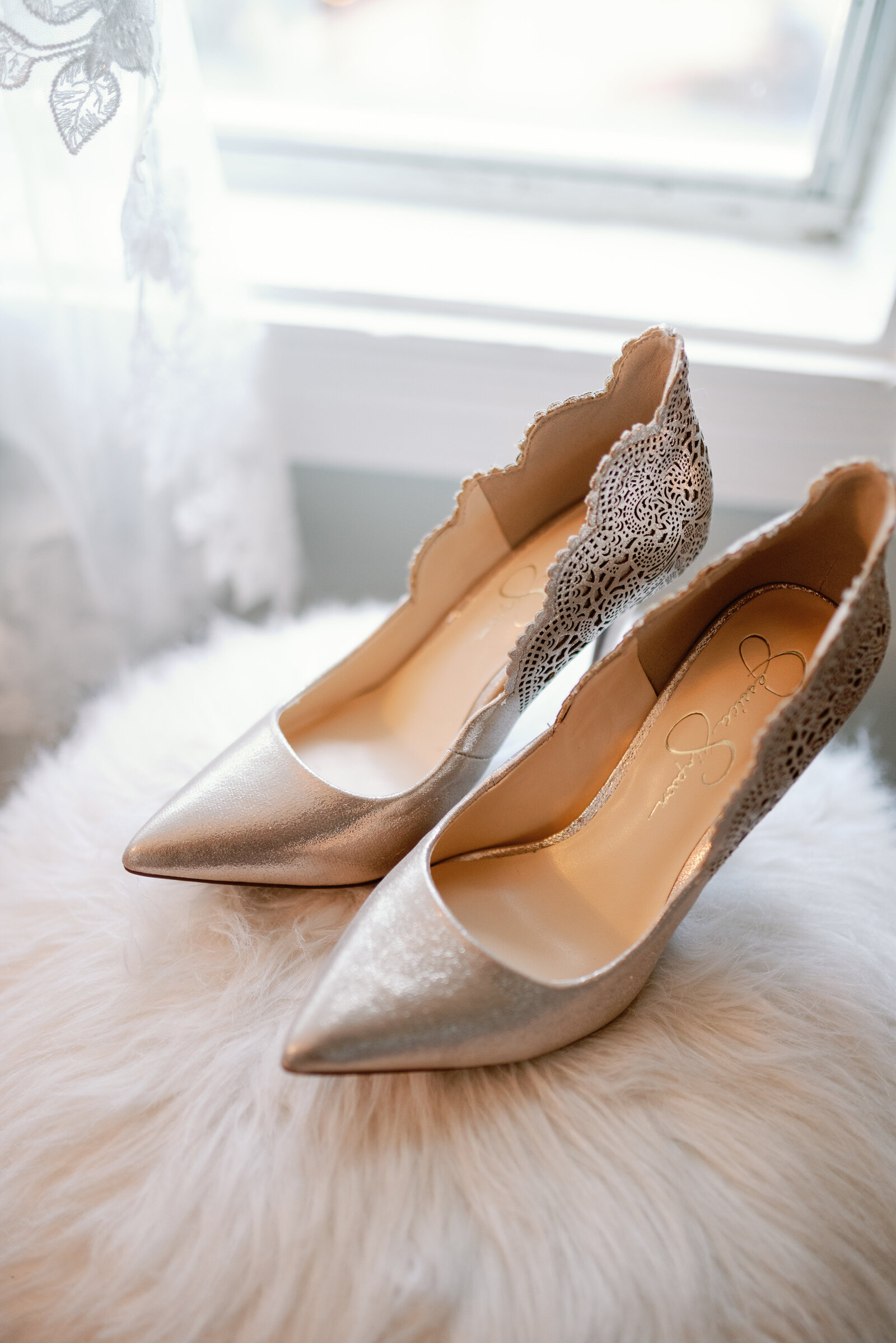 Brides wedding day shoes sitting in front of a bright window on a fluffy stool